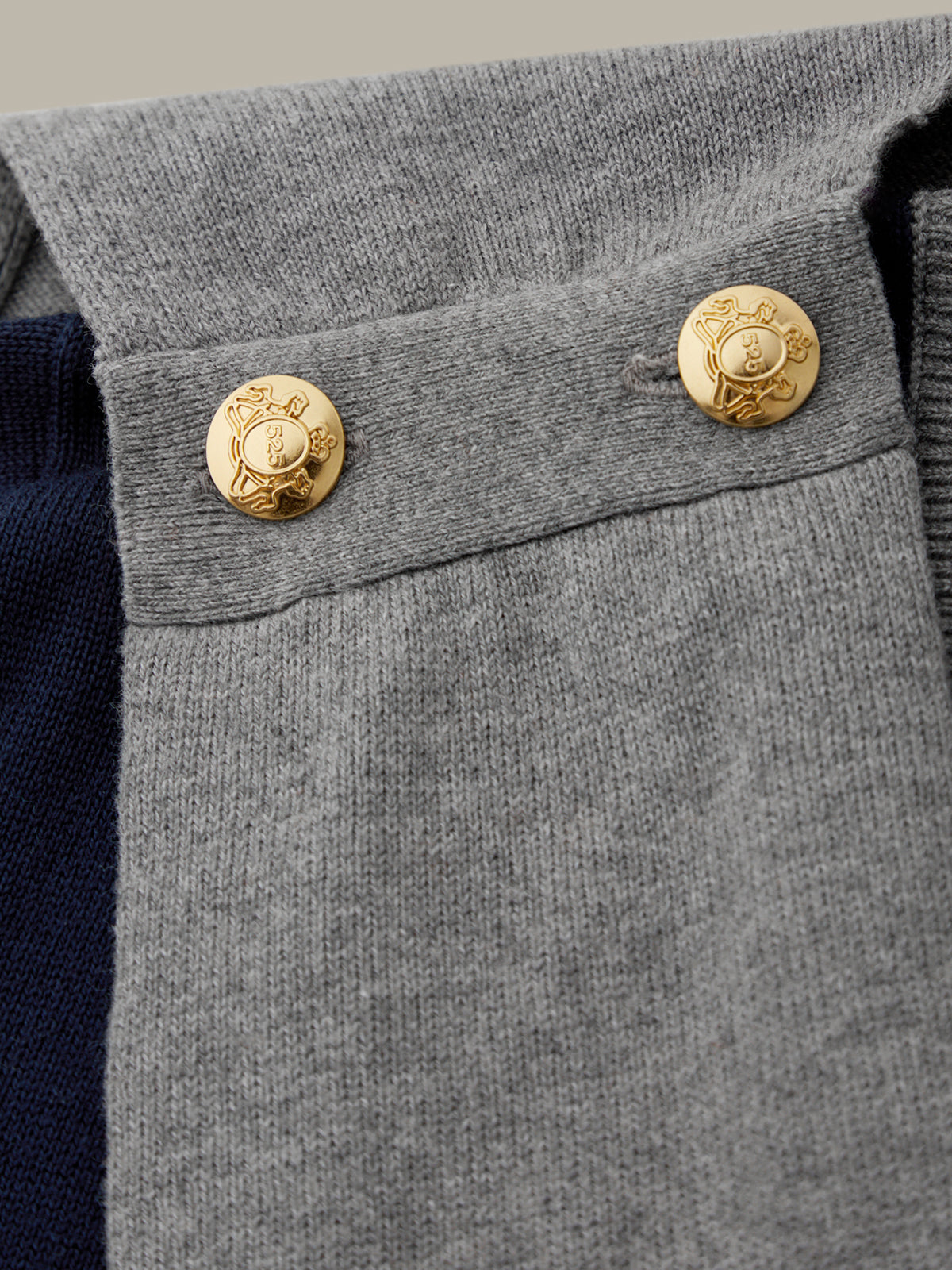 Close-up of a gray garment with gold buttons featuring a logo.