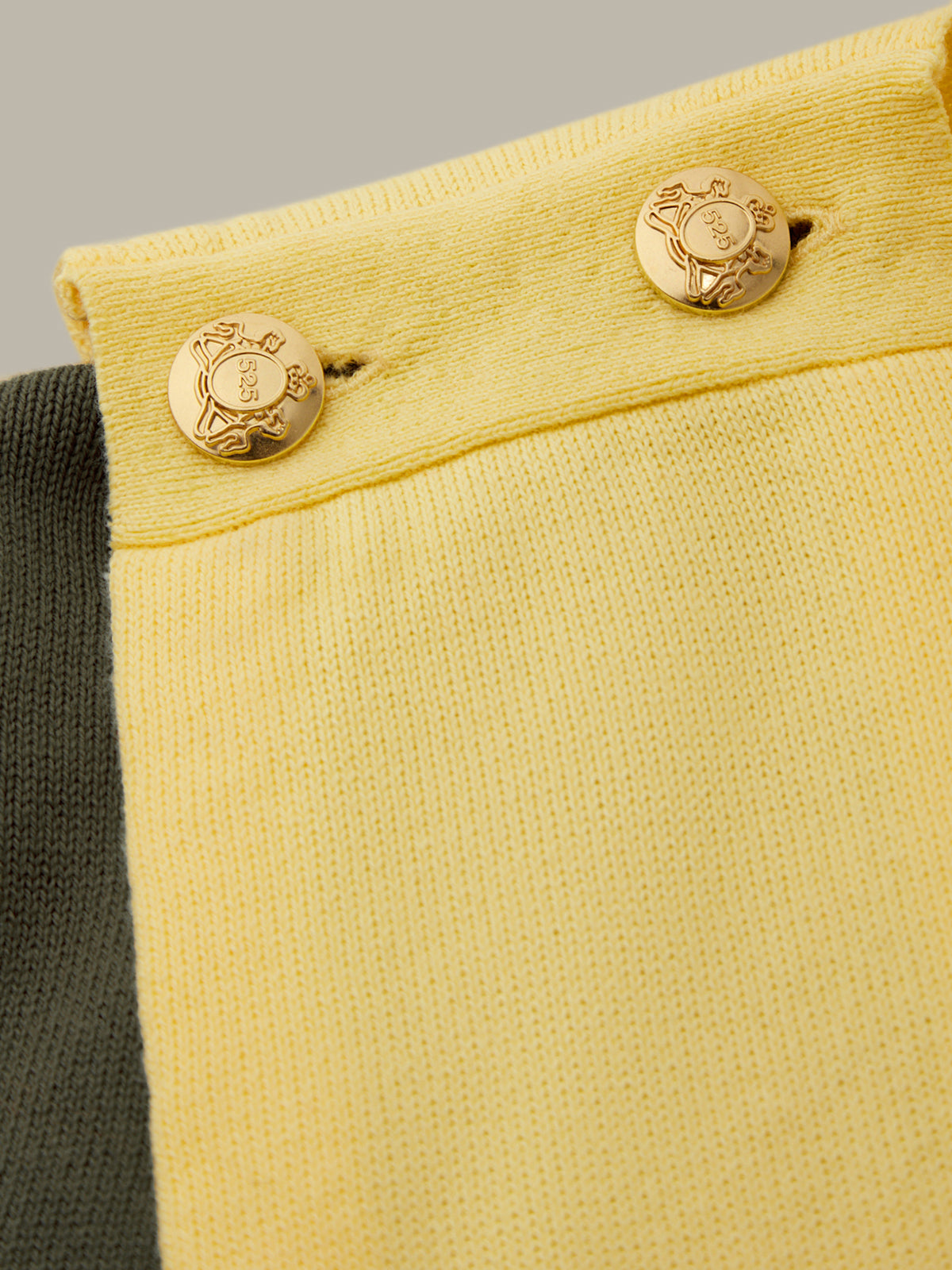 Close-up of a yellow fabric with gold buttons on a neutral background