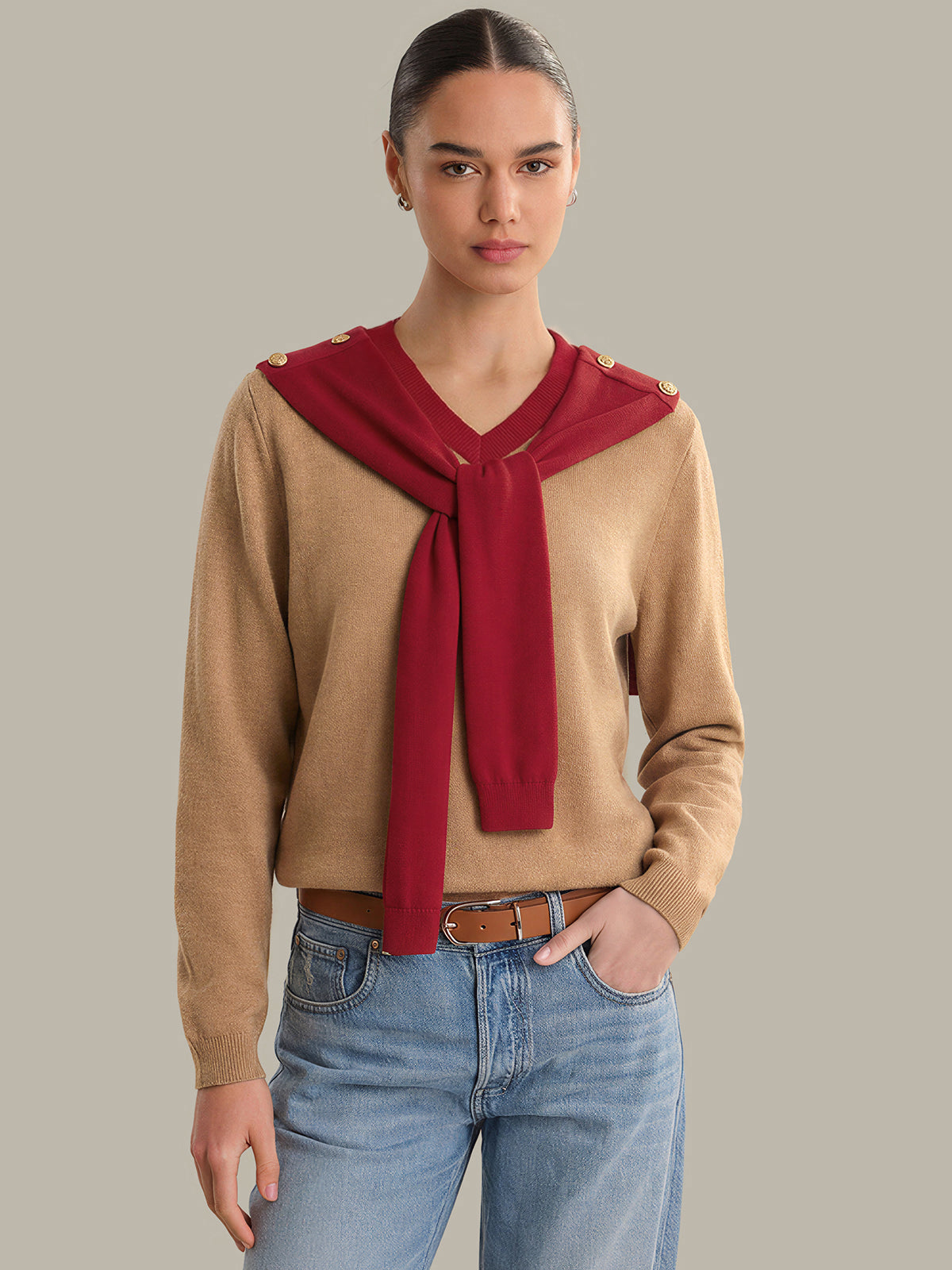 Woman wearing a beige sweater with a red scarf and blue jeans on a gray background
