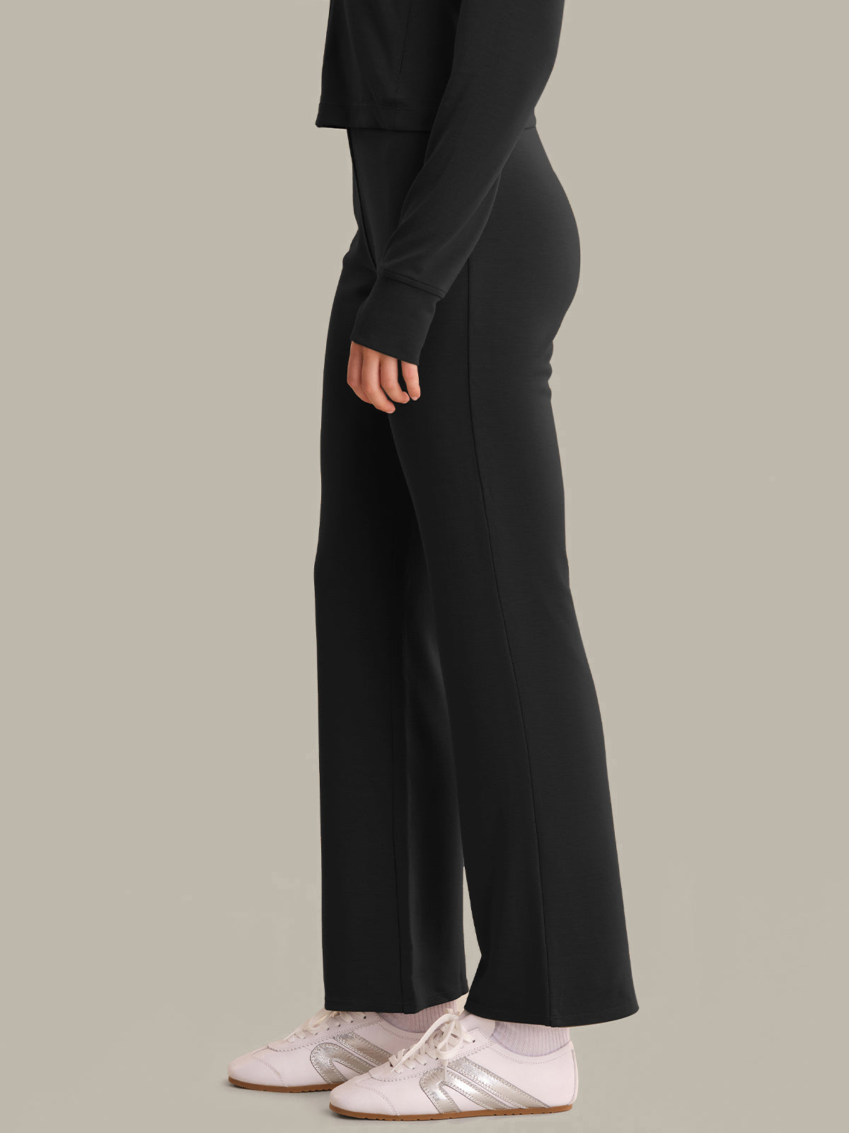 Person wearing black wide-leg pants and white sneakers on a plain background