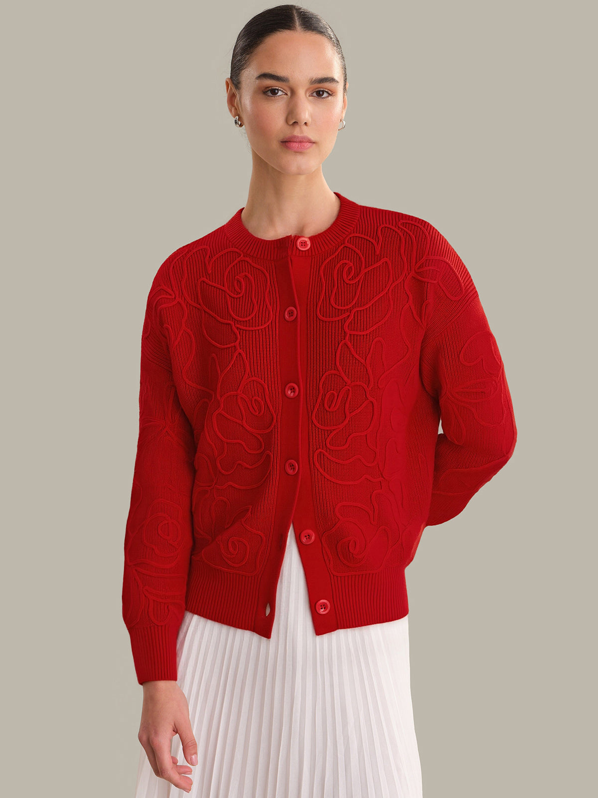 Woman wearing a red cardigan with intricate patterns on a plain background