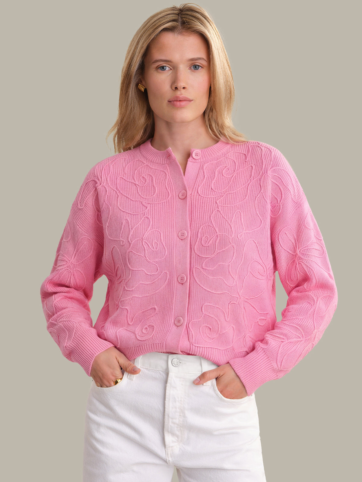 Woman wearing a pink cardigan with a subtle pattern against a plain background