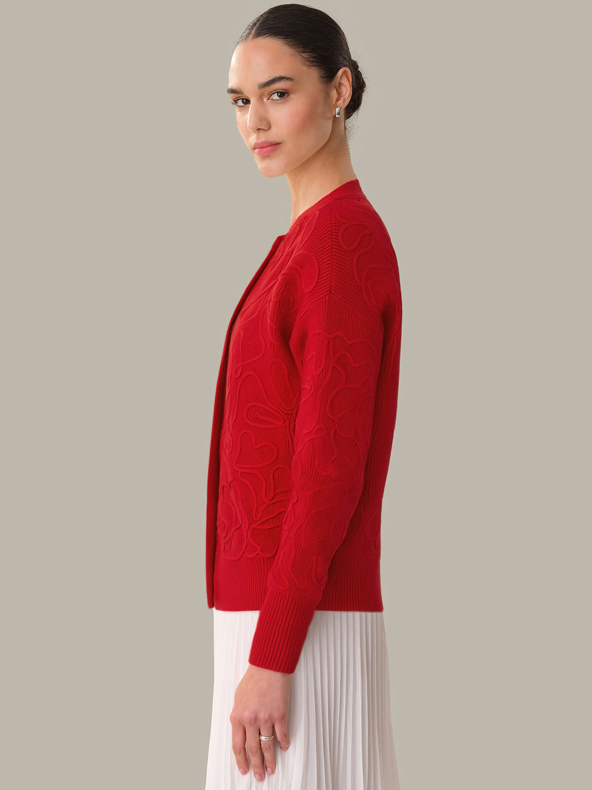 Woman wearing a red cable knit cardigan against a plain background