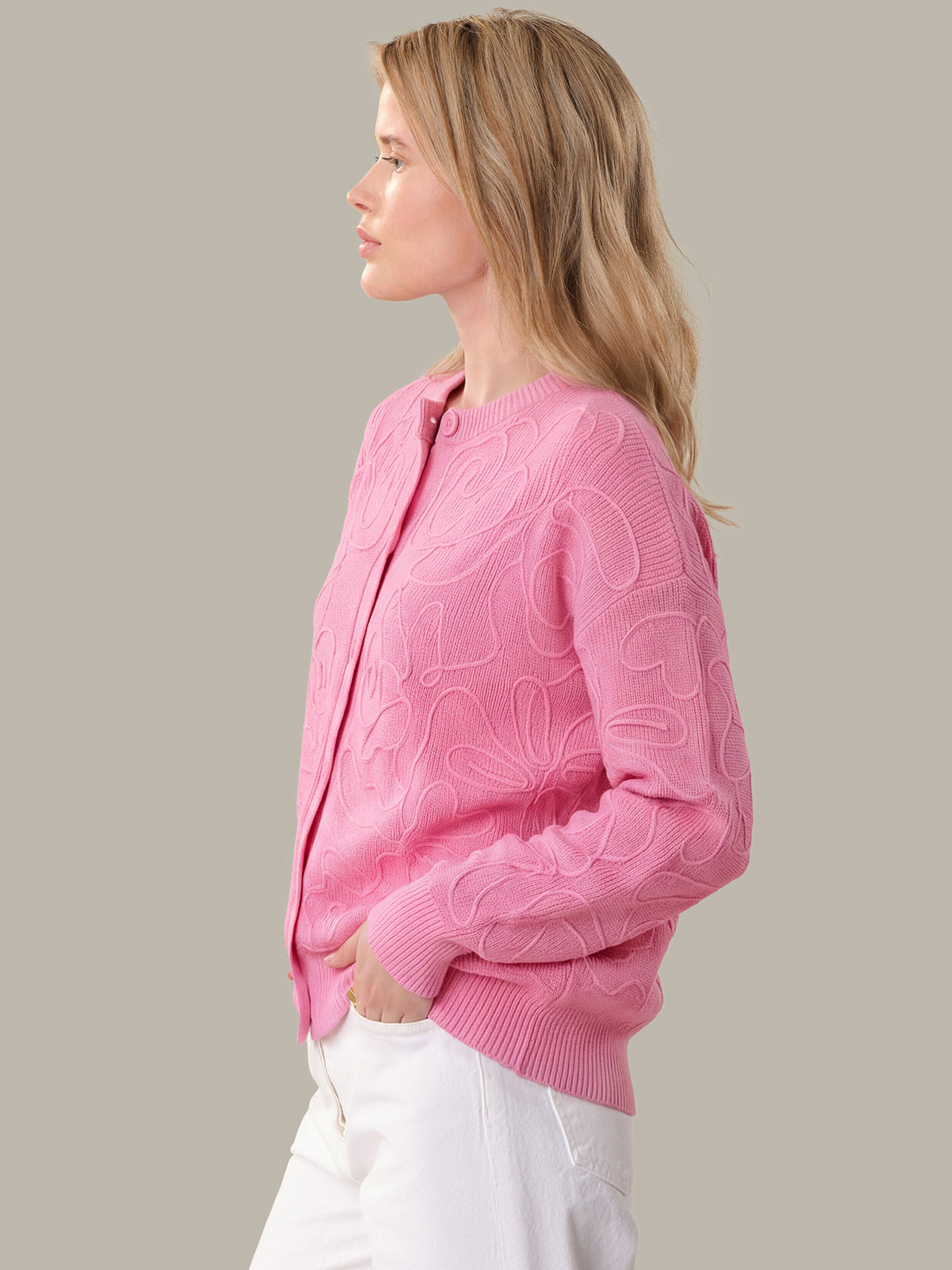 Woman wearing a pink sweater with a subtle pattern on a plain background