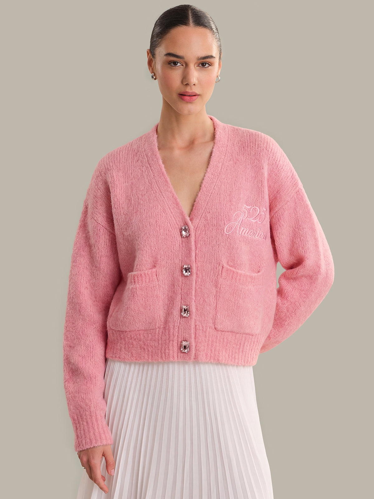 Woman wearing a pink cardigan with a brand logo on a gray background
