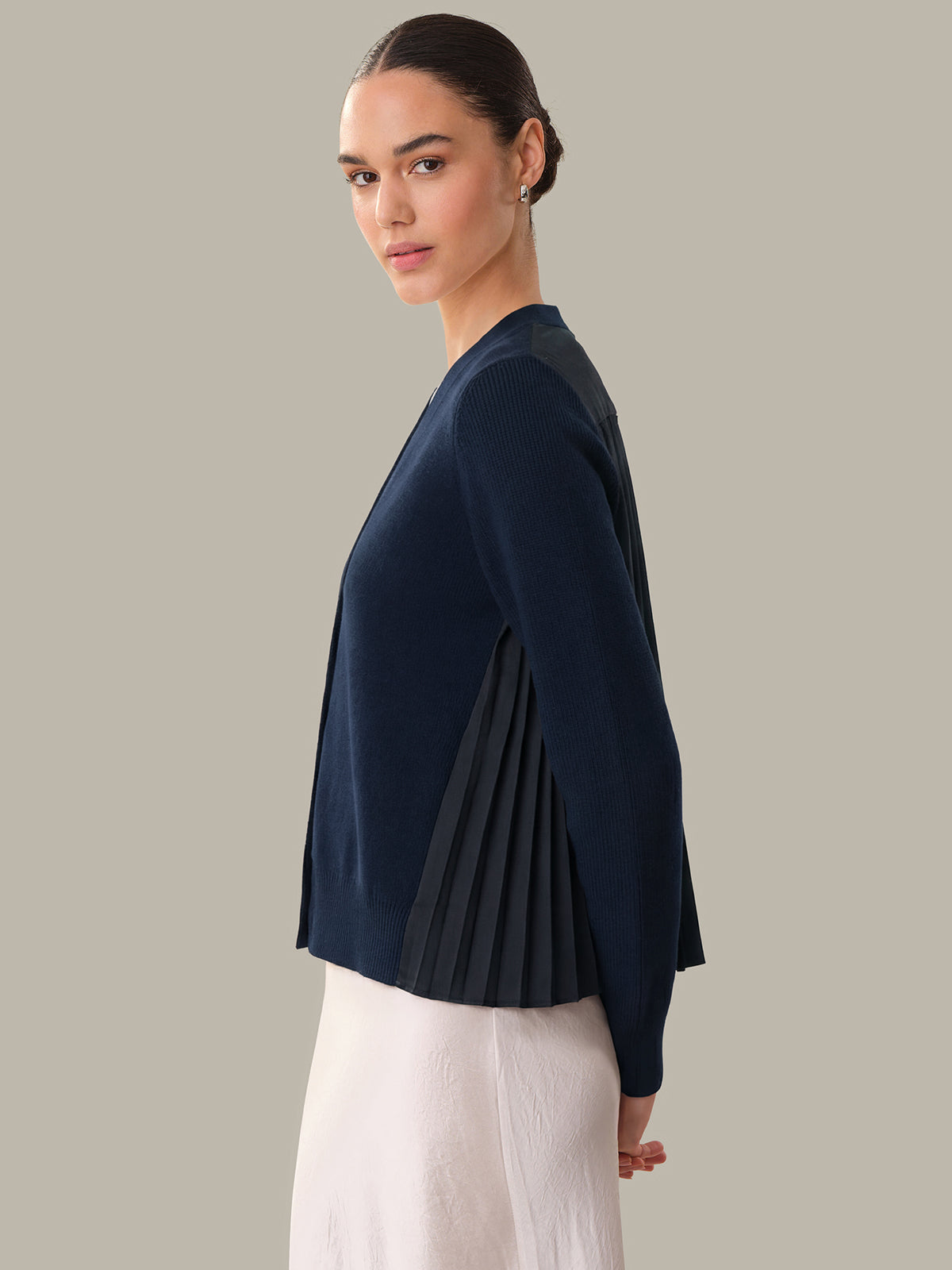 Woman wearing a navy blue cardigan with pleated details on a gray background