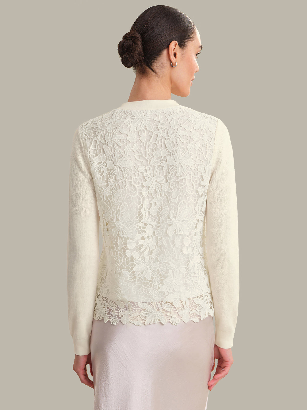 Woman wearing a cream lace cardigan against a plain background