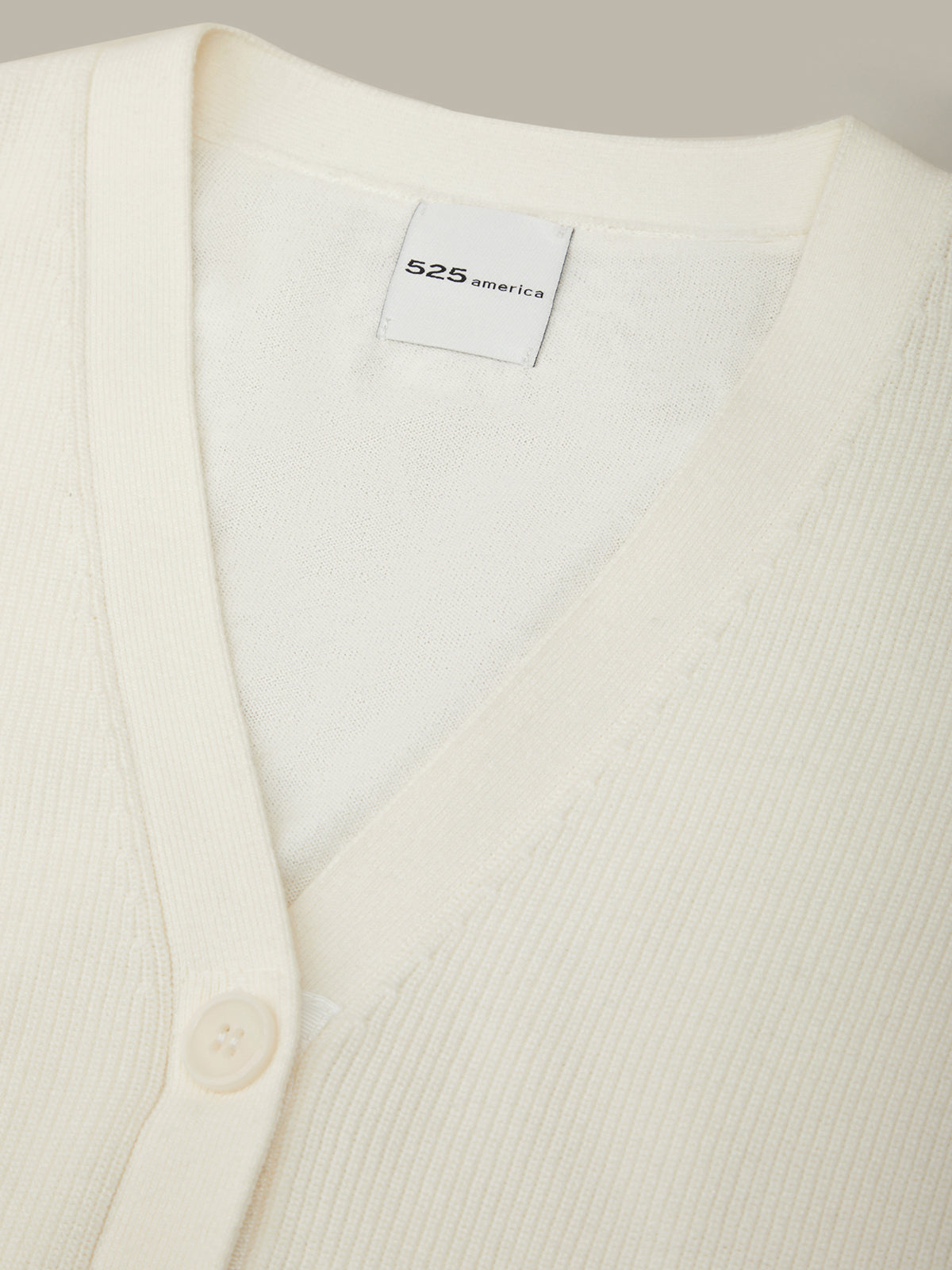 Close-up of a white cardigan with a brand label on a neutral background