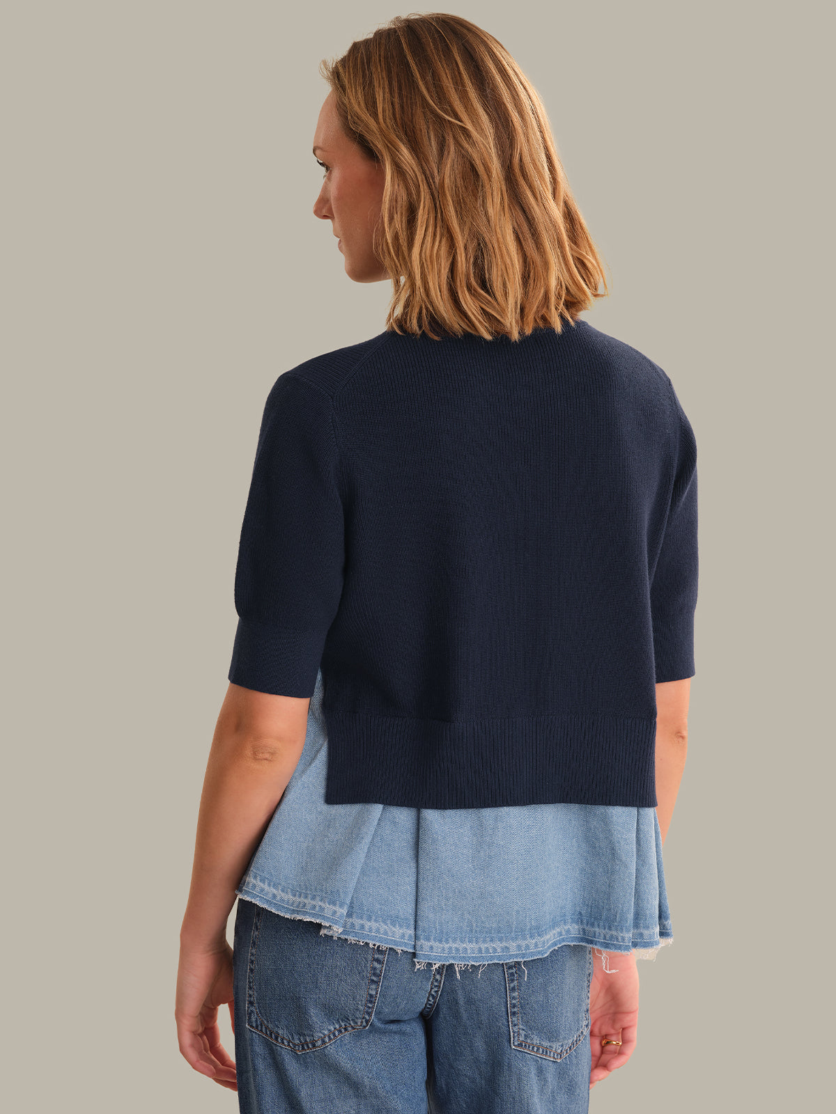 Woman wearing a navy sweater over a light blue shirt with jeans on a plain background