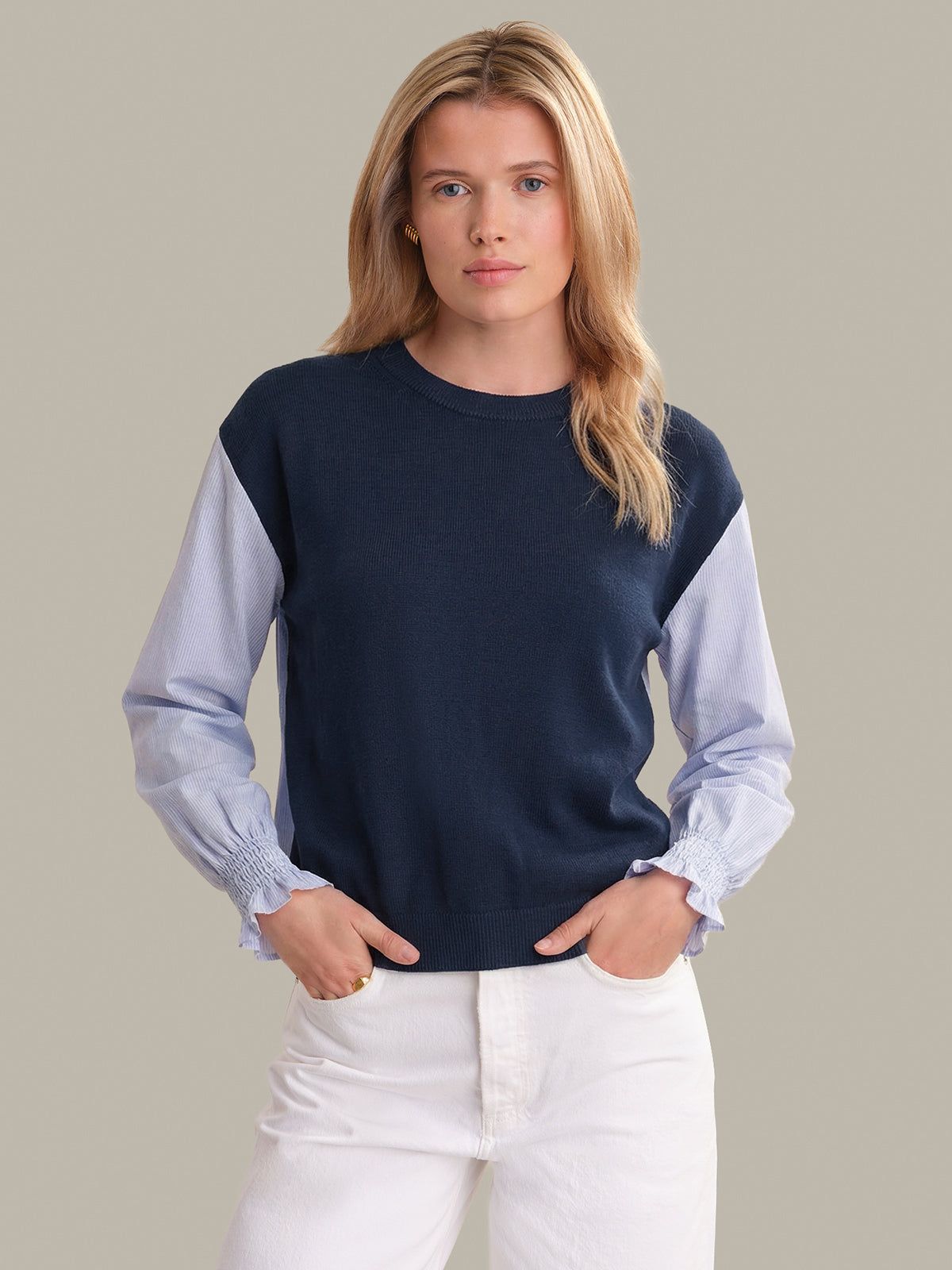 Woman wearing a navy and light blue sweater with white pants on a plain background