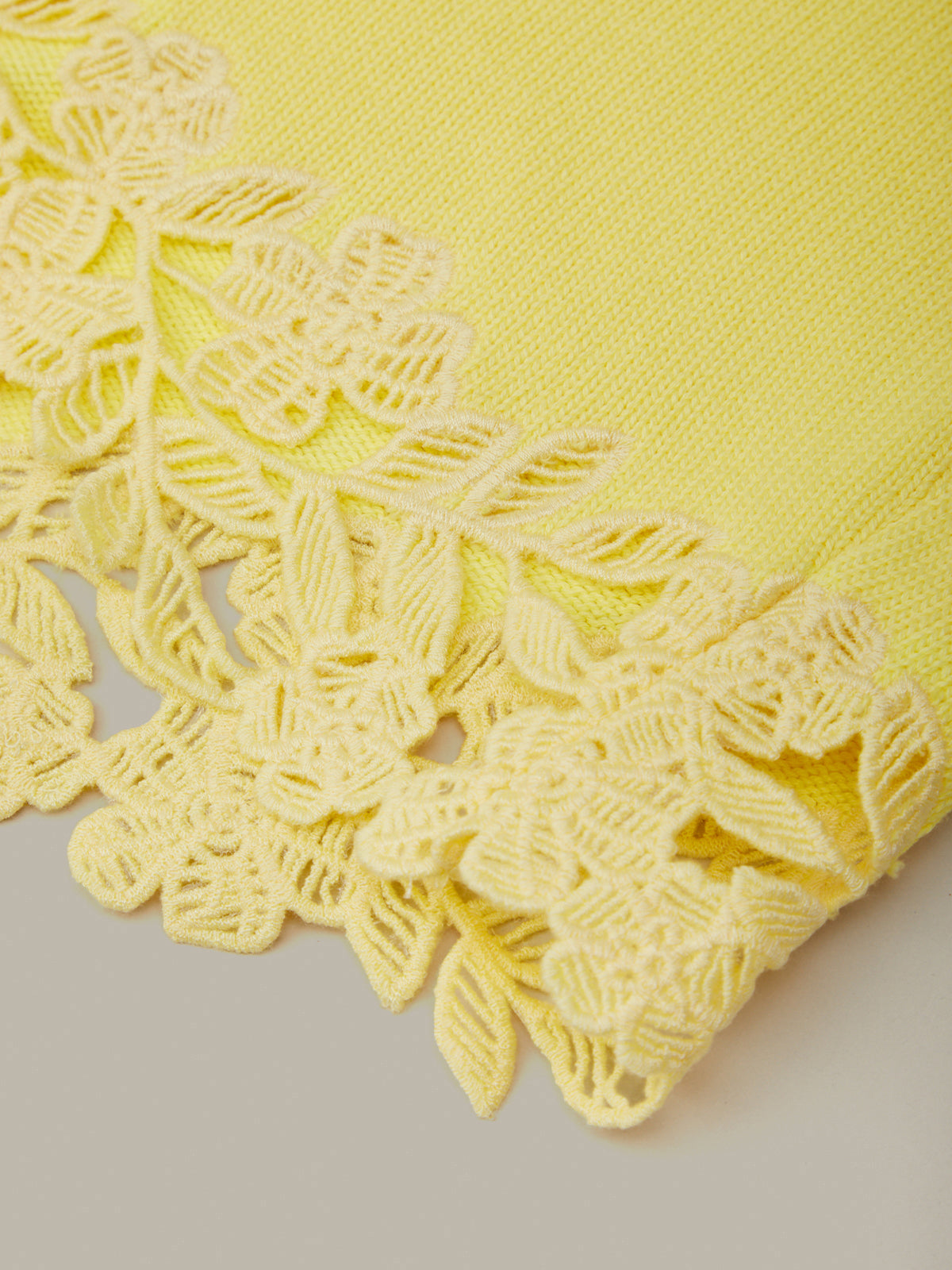 Yellow fabric with intricate lace detailing on a neutral background