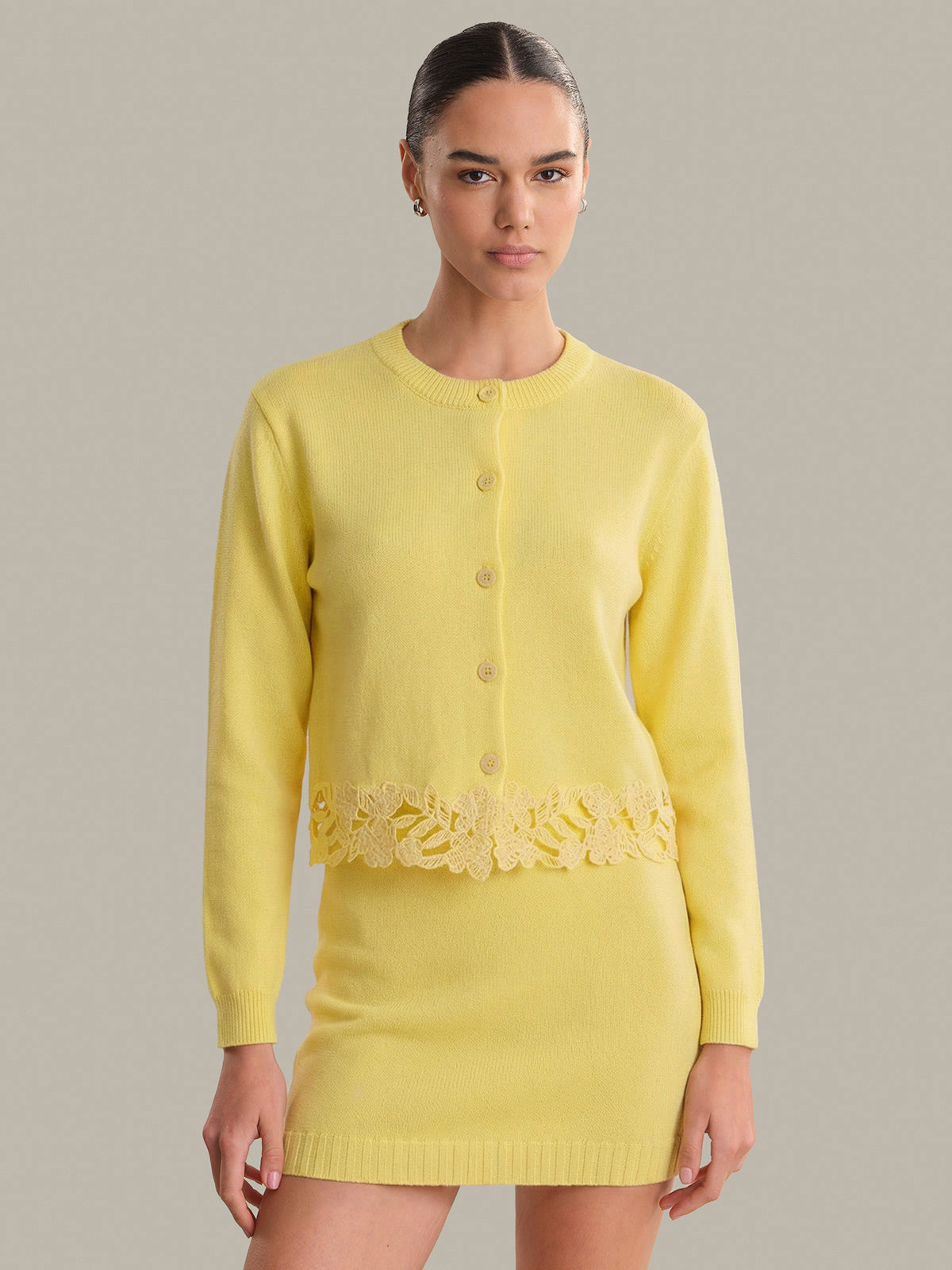 Woman wearing a yellow outfit with lace details on a gray background