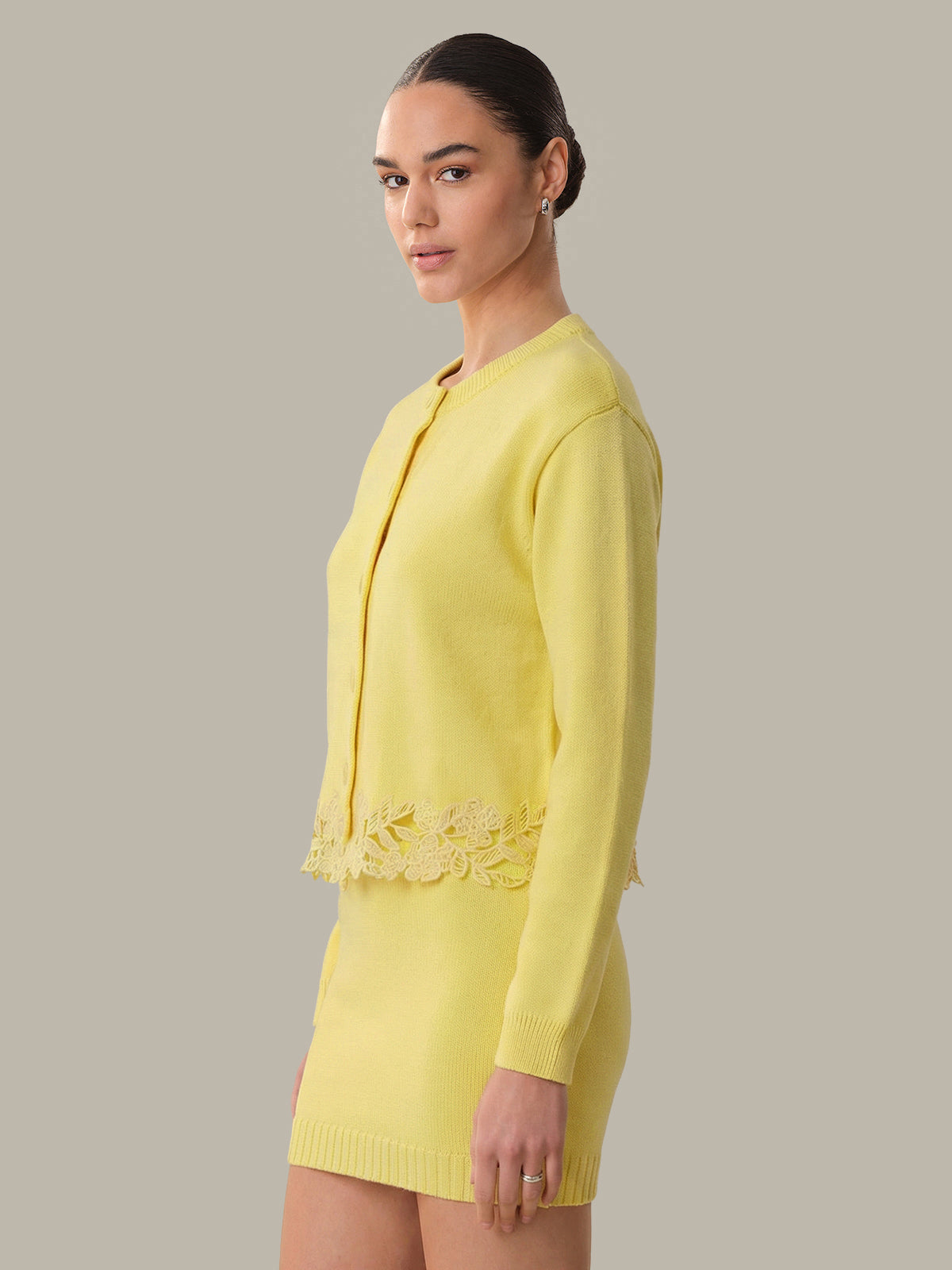 Woman wearing a yellow suit with lace details on a plain background