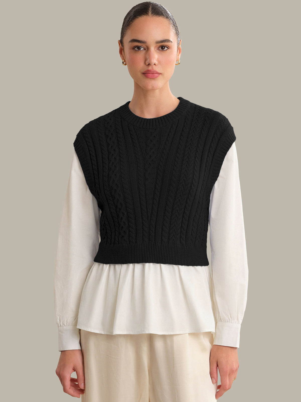 Person wearing a black knitted vest over a white long-sleeve shirt on a neutral background