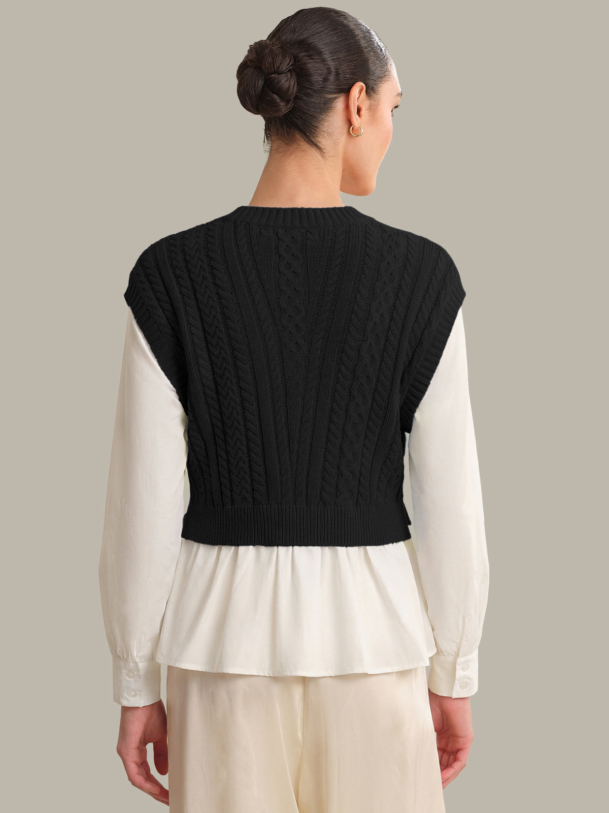 Person wearing a black knitted vest over a white shirt on a neutral background