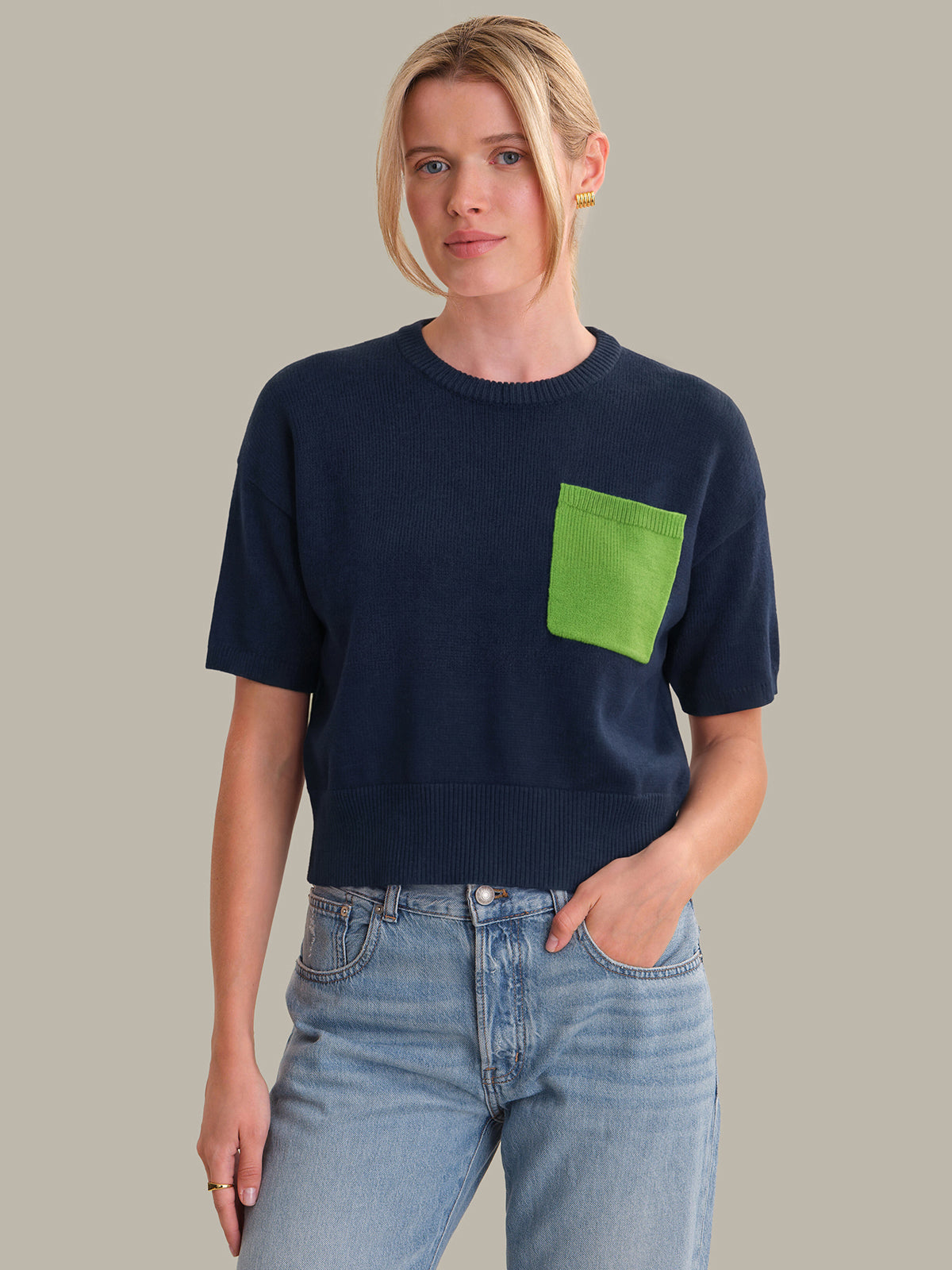 Person wearing a navy blue sweater with a green pocket on a plain background