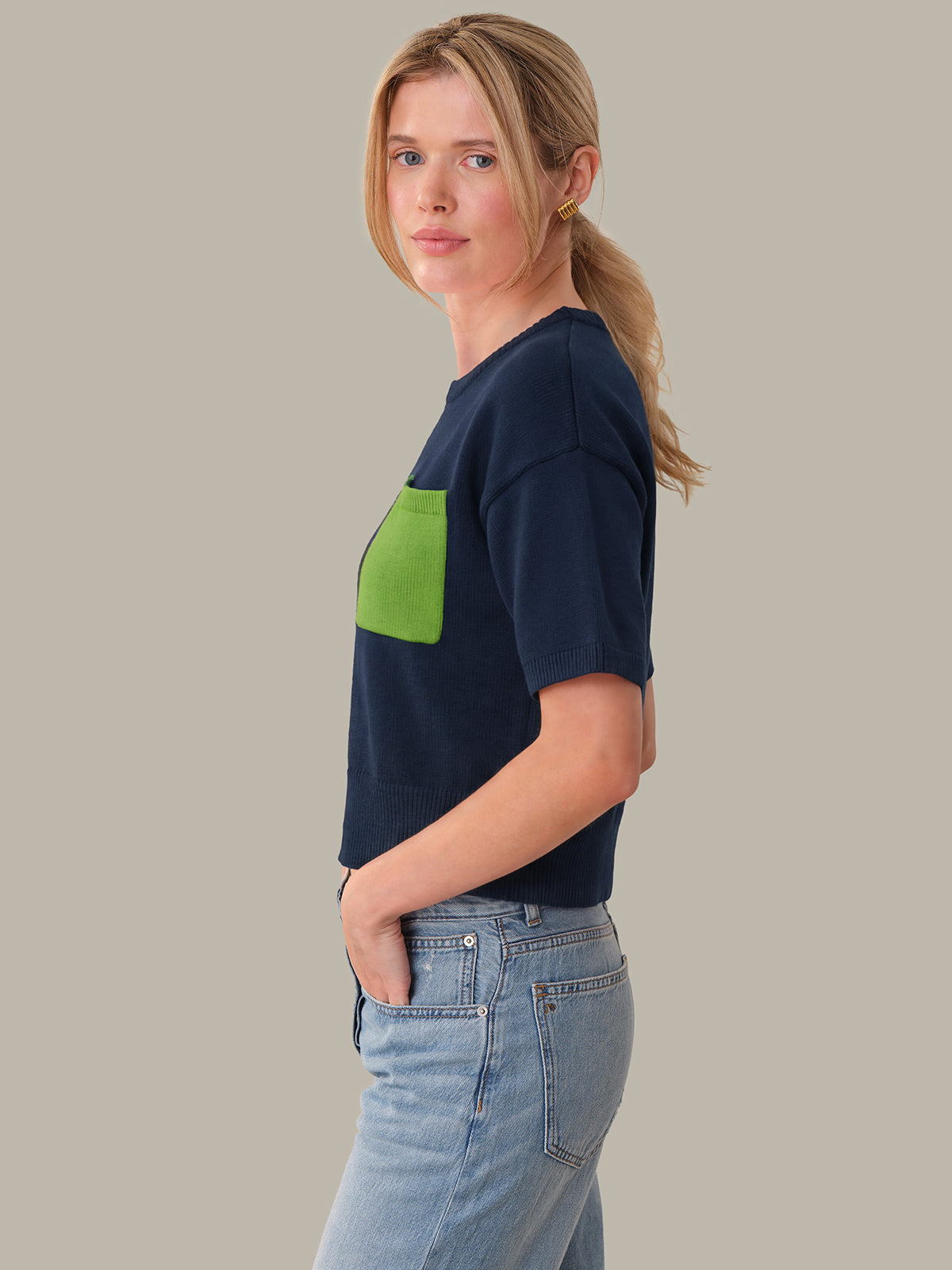 Woman wearing a navy t-shirt with a green pocket on a plain background