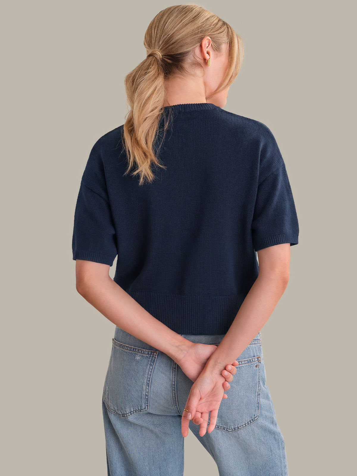Person wearing a navy sweater and light blue jeans on a plain background