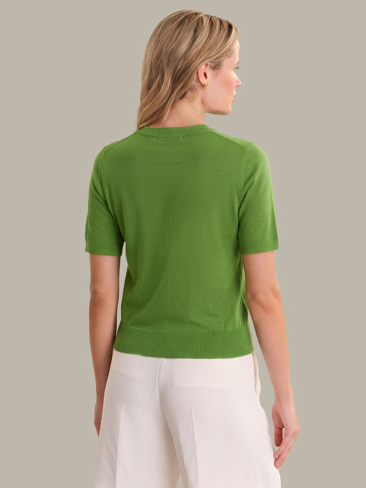 Woman wearing a green sweater and white pants against a gray background