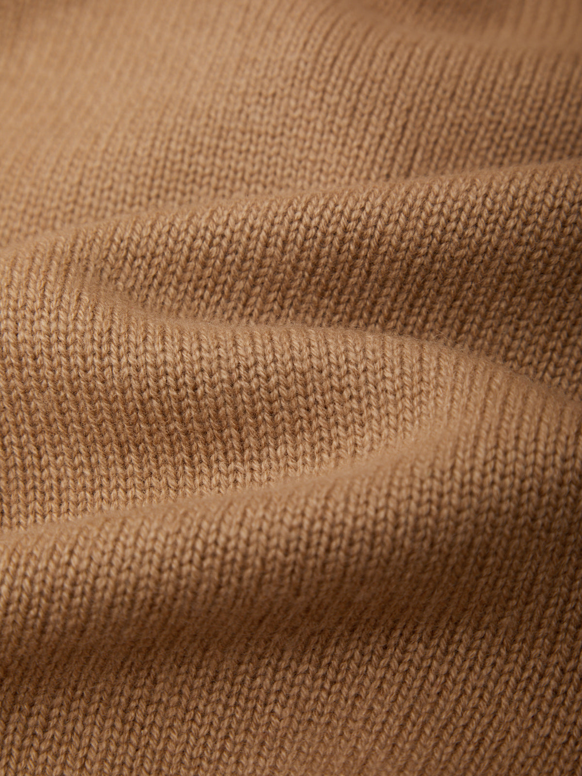 Close-up of a warm camel brown knit fabric with a fine ribbed texture and soft folds.