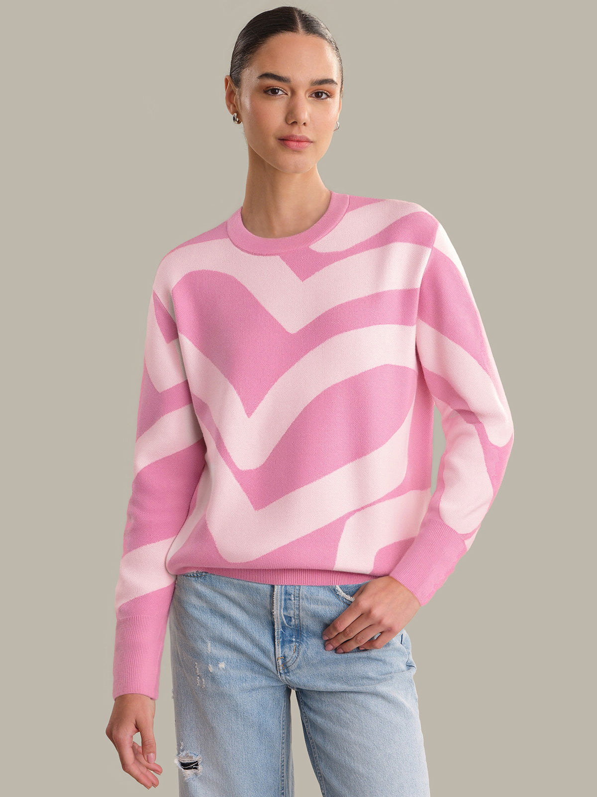 Person wearing a pink and white patterned sweater with light blue jeans on a neutral background
