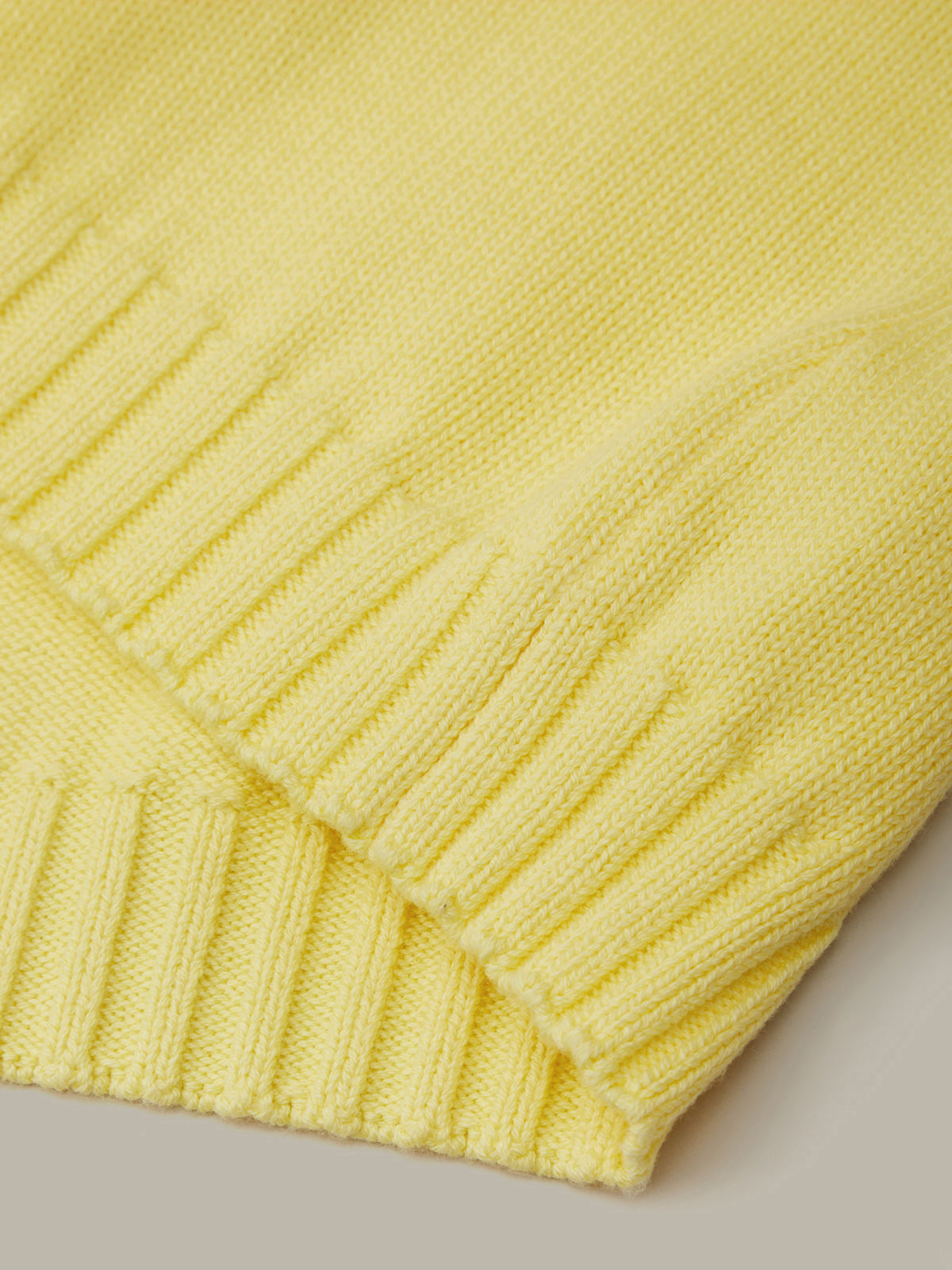 Close-up of a yellow knitted sweater on a light gray background