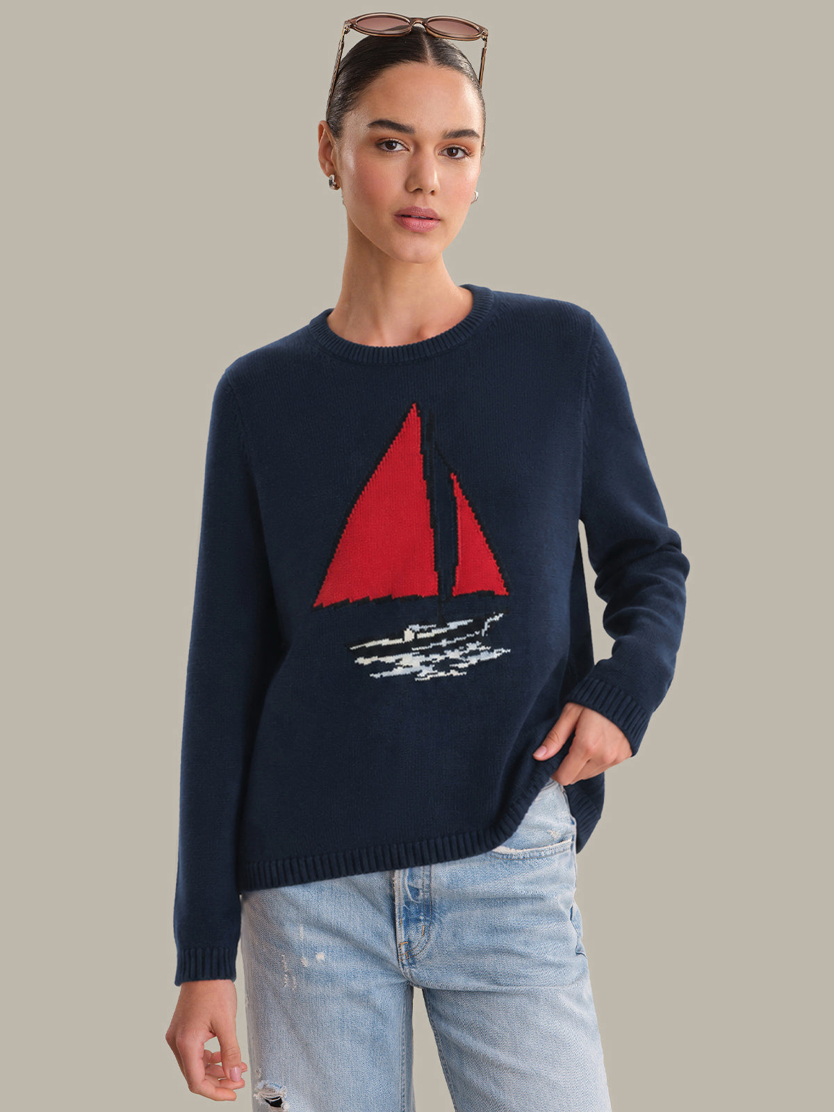Woman wearing a navy sweater with a red sailboat design on a plain background