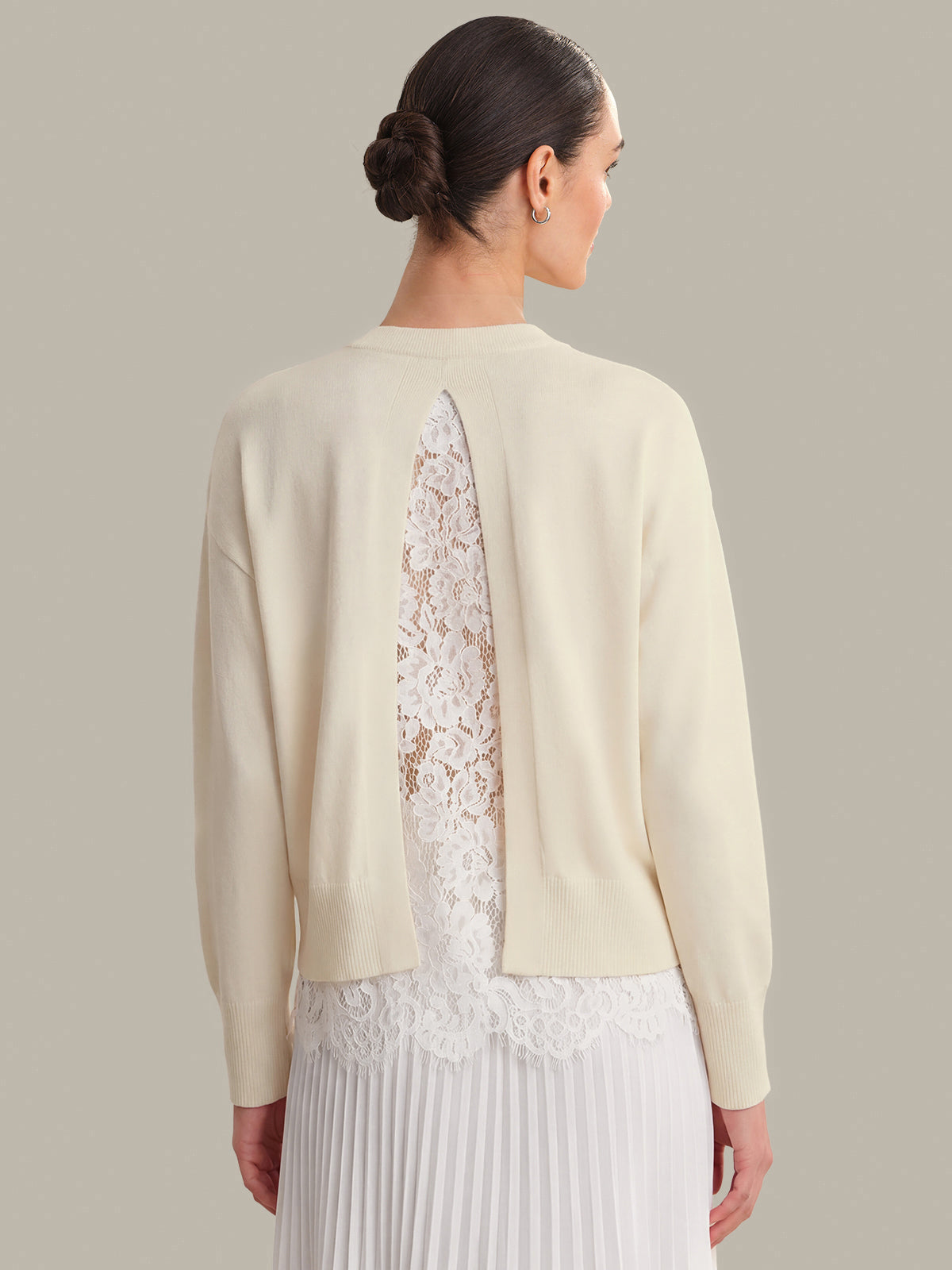 Woman wearing a cream cardigan with lace detailing on a plain background