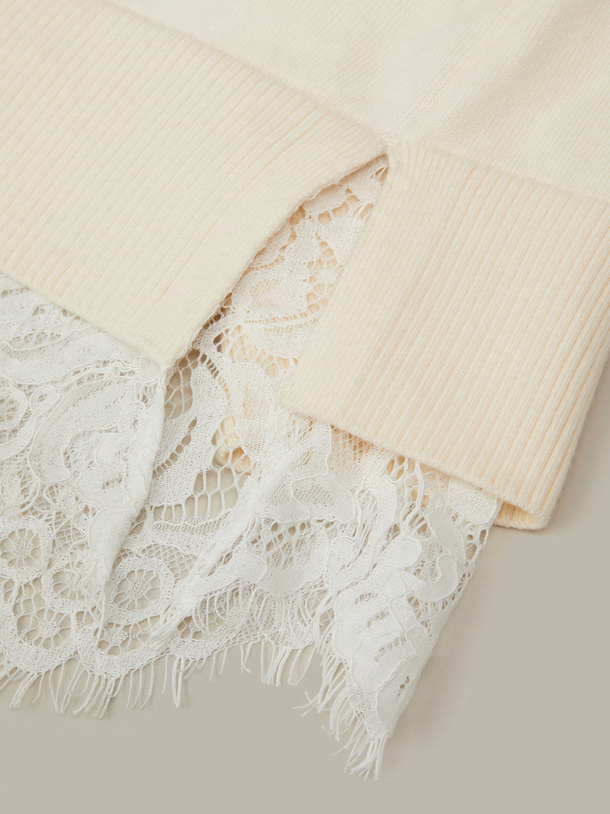 Close-up of a beige sweater with lace trim on a neutral background