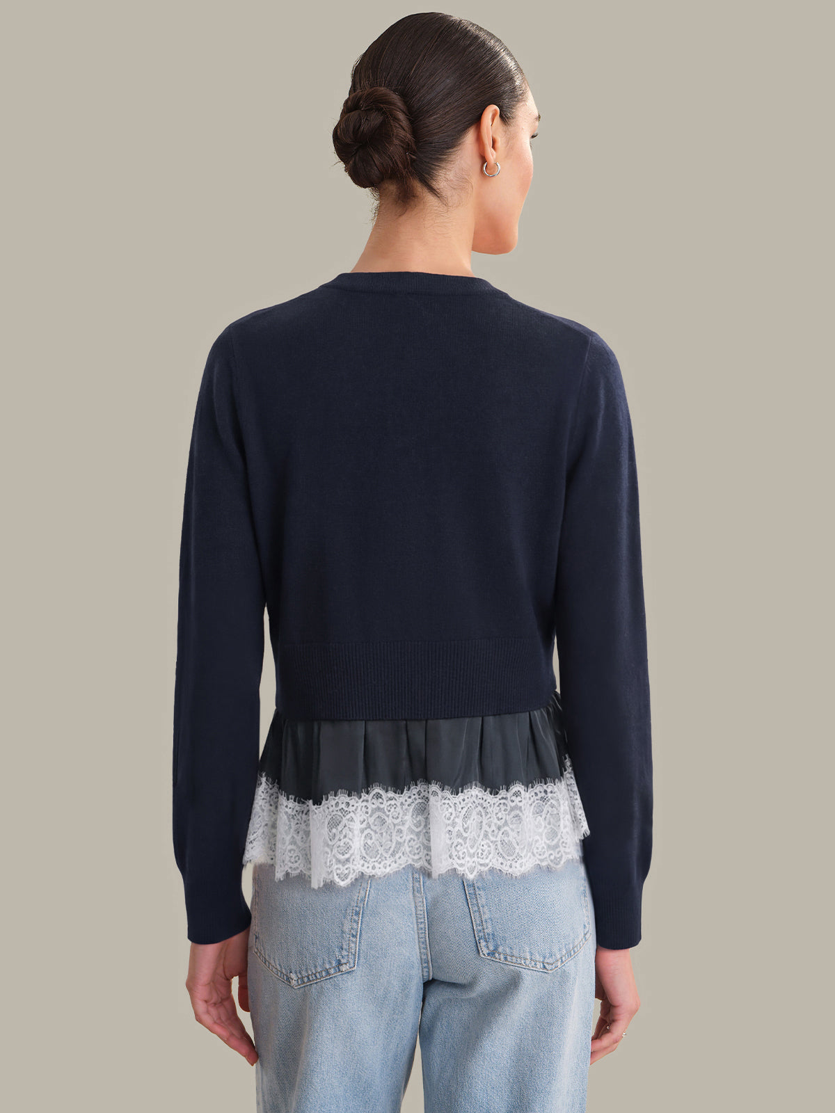 Person wearing a navy blue sweater with lace trim on a plain background
