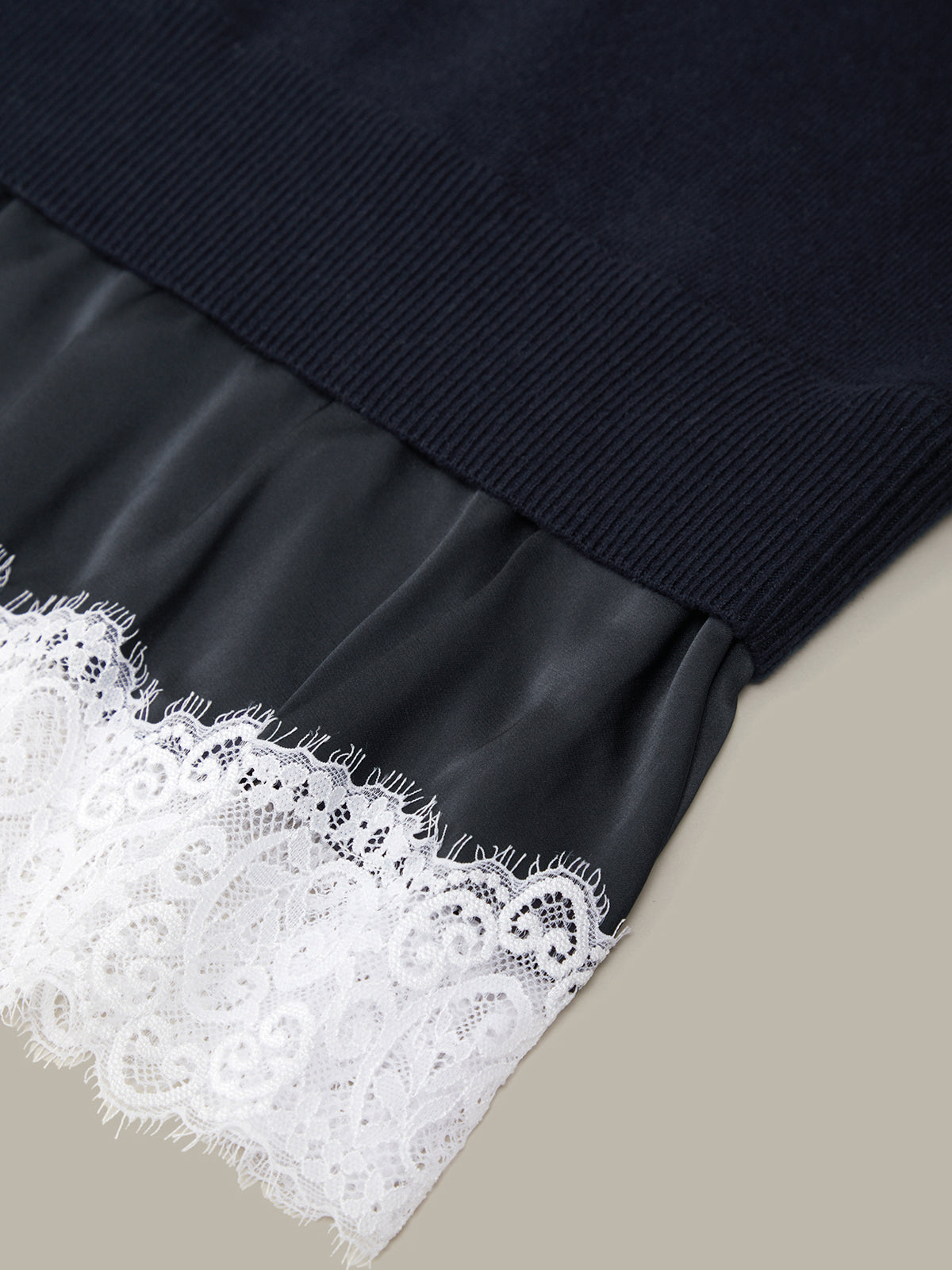 Navy sweater with a black leather-like trim and white lace detailing on a beige background