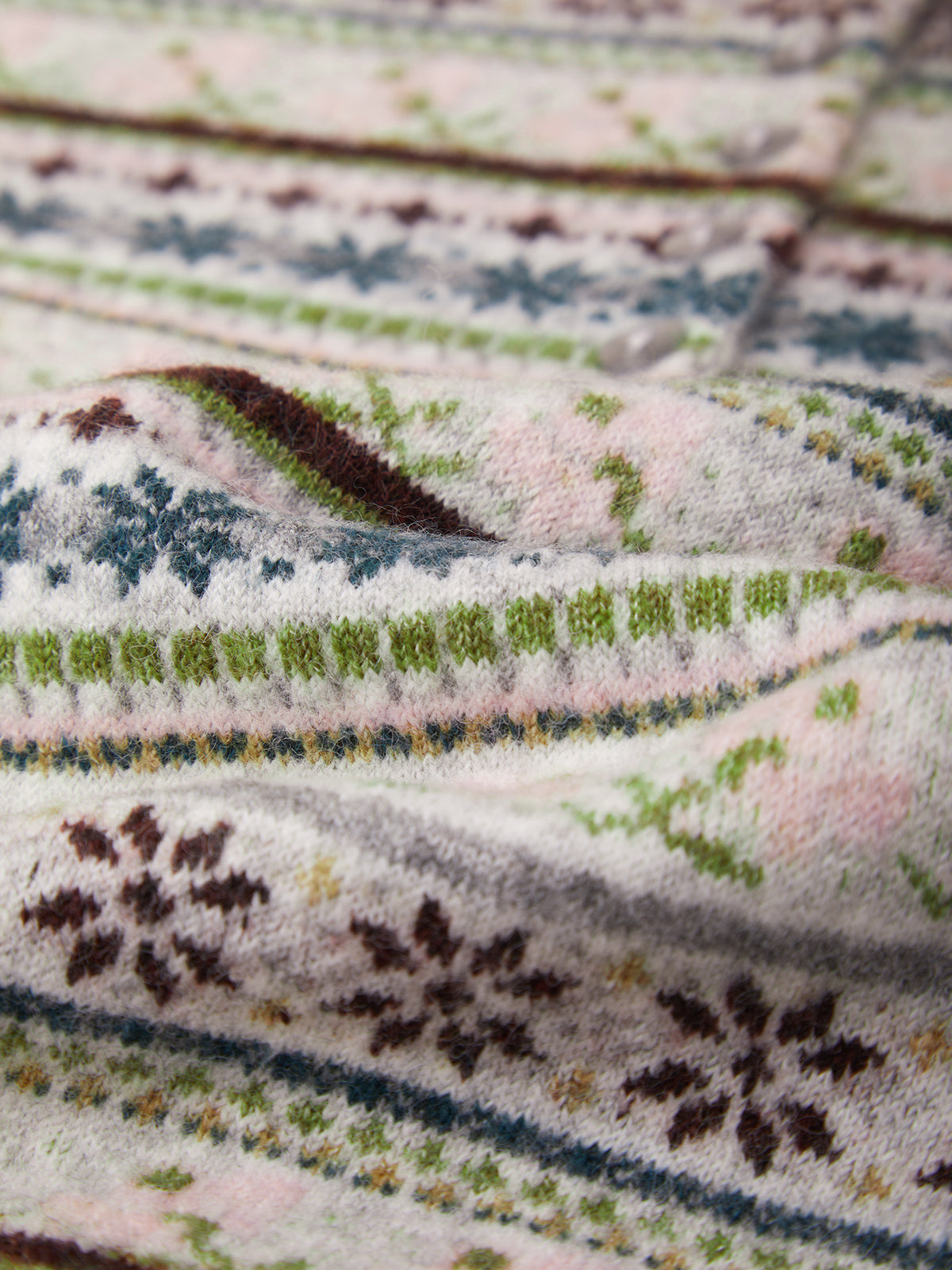 A close-up of a soft knit fabric with a Fair Isle style pattern featuring pink, green, blue, and brown motifs on a cream background.