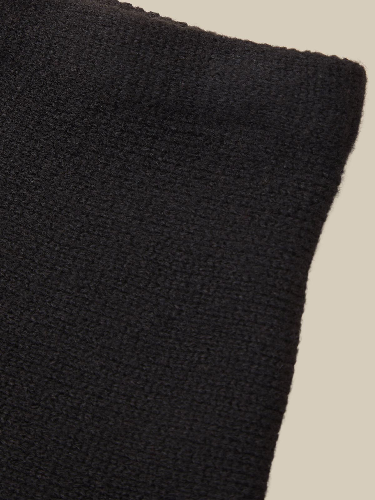 Close-up of a black ribbed knit fabric texture against a light beige background.