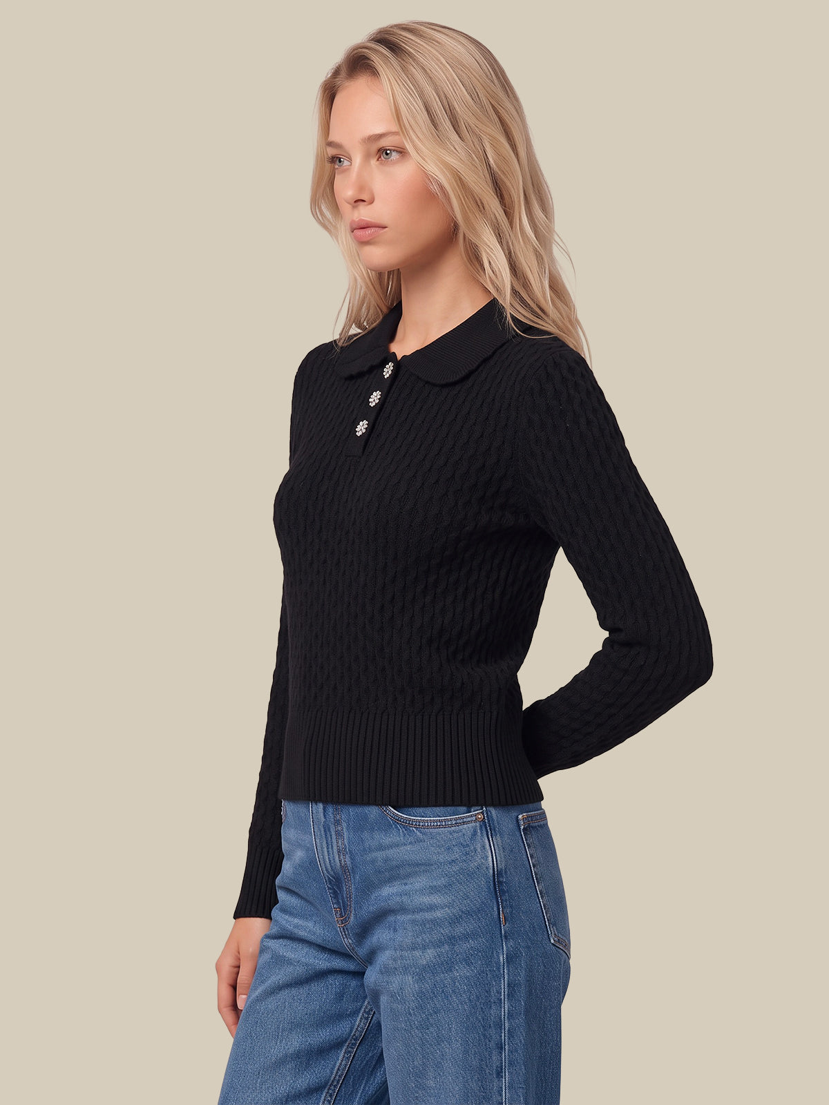 A woman wearing a black ribbed knit polo sweater with a small button placket and blue jeans, photographed against a plain beige studio background.