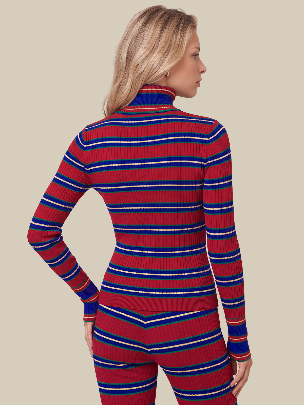 A woman shown from the back wearing a fitted ribbed turtleneck sweater and matching pants with horizontal red, blue, and white stripes, against a plain beige studio background.