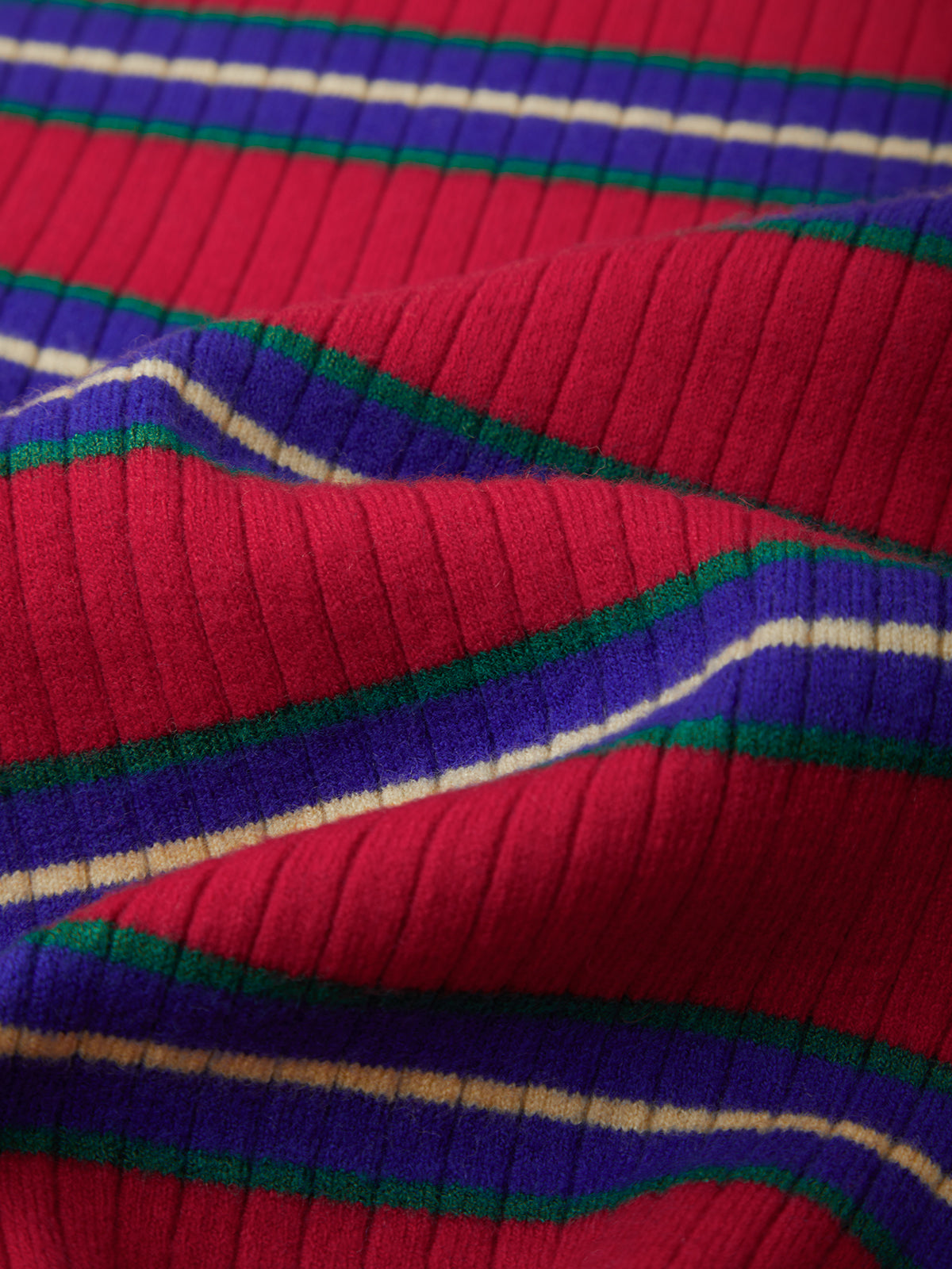A close-up of a ribbed knit fabric with a bold multicolor stripe pattern featuring red, purple, green, and cream stripes.