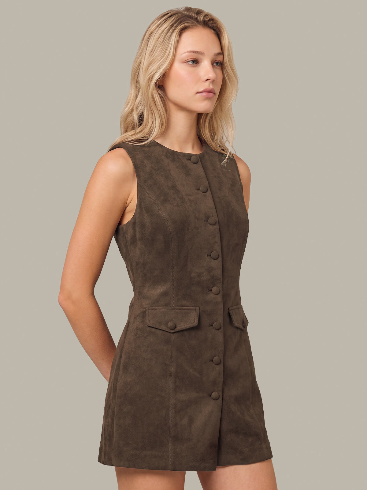 A blonde woman modeling a sleeveless dark brown faux-suede romper with a button-front detail and flap pockets, set against a solid light gray background.