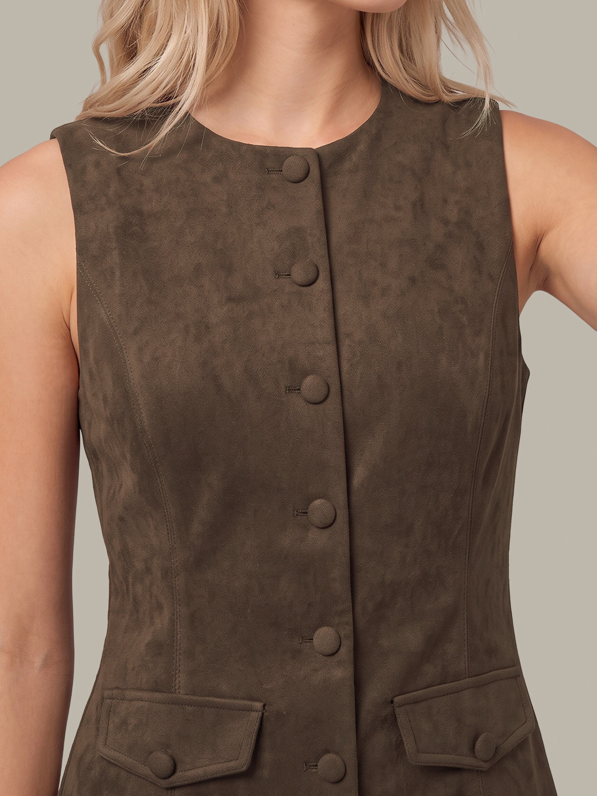 Close-up of a woman wearing a sleeveless dark brown suede-like vest with a button front and flap pockets, against a plain light gray background.