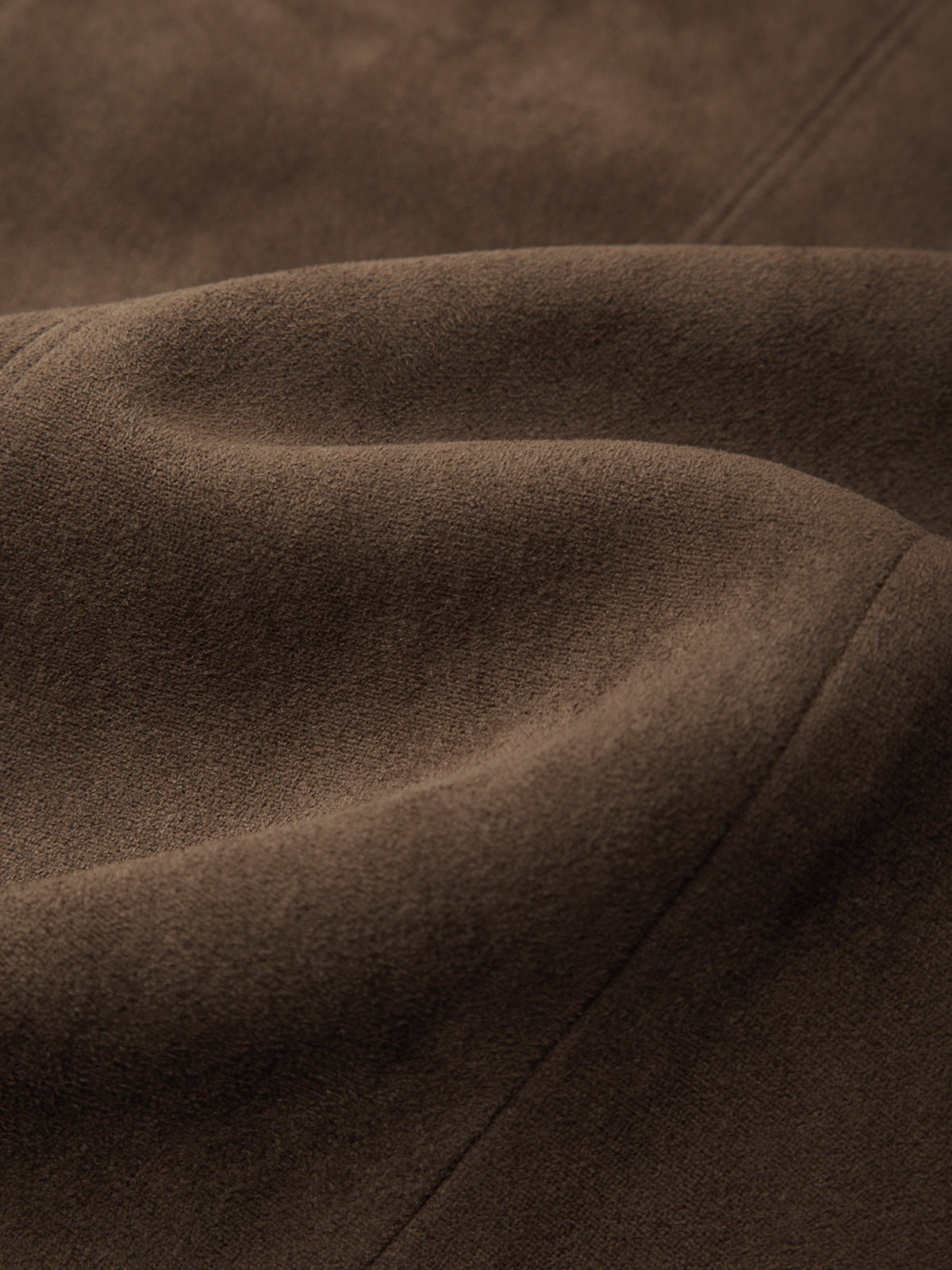 A close-up of draped brown suede fabric with soft folds and a matte texture.