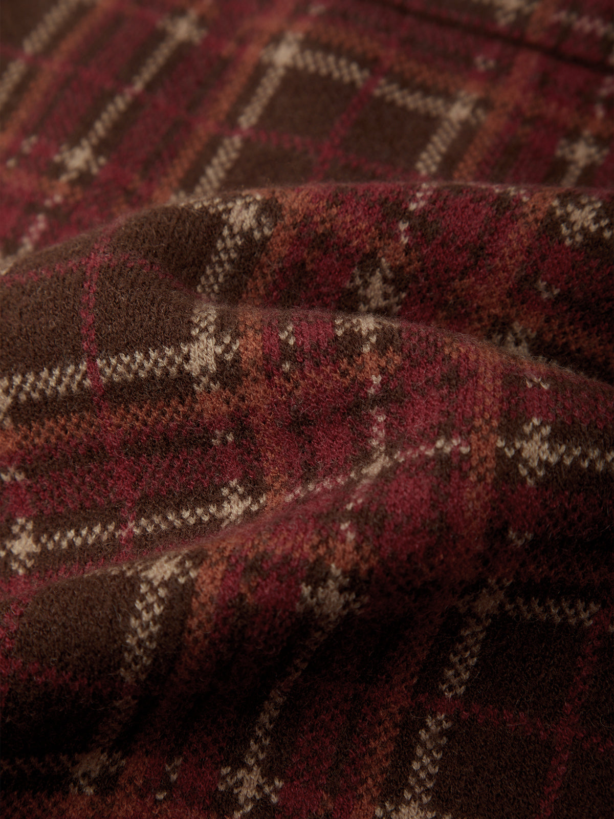 A close-up of a textured knit fabric with a plaid pattern in deep burgundy red, dark brown, and cream.