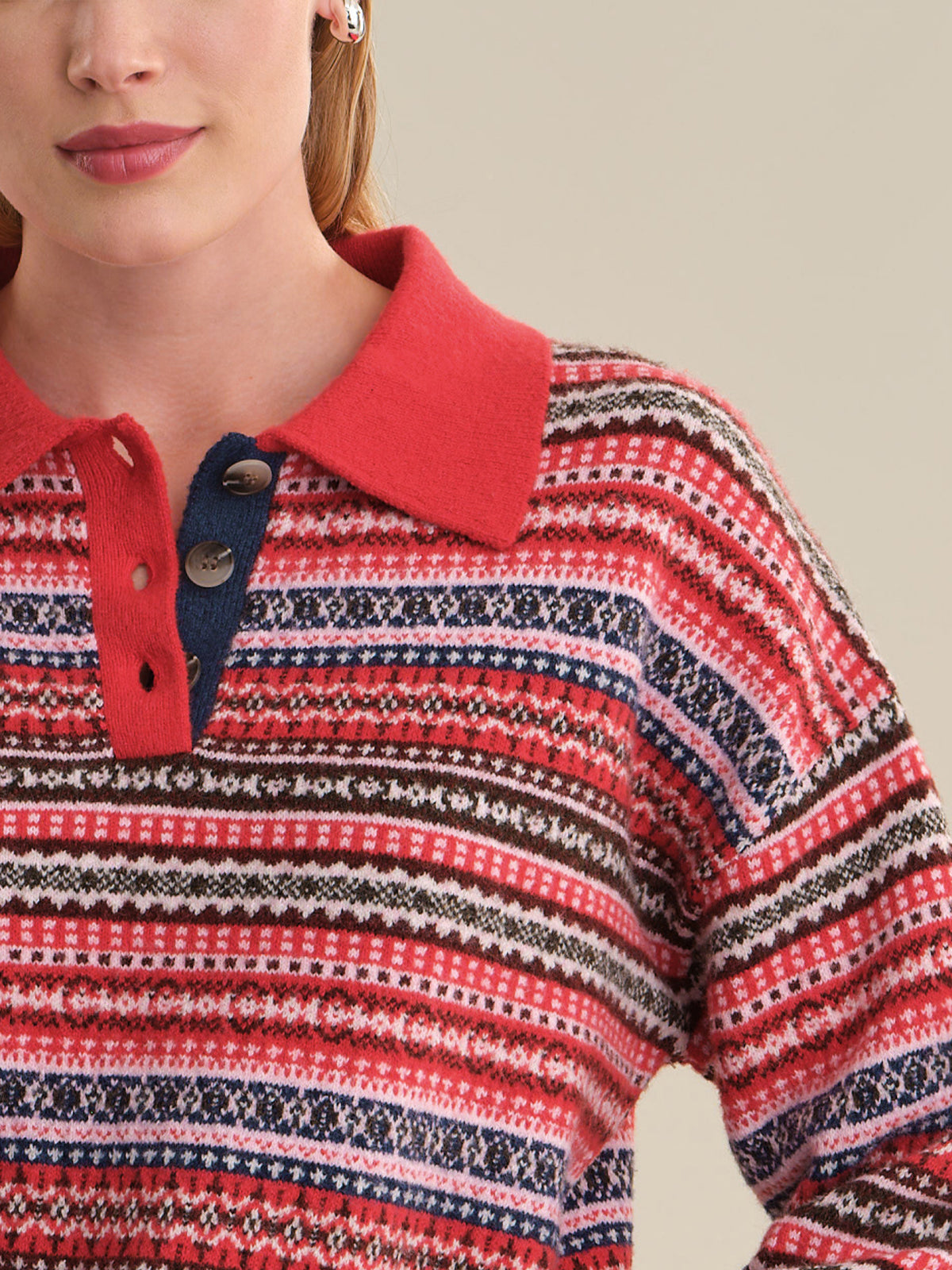 Close-up of a woman wearing a knit polo sweater with horizontal Fair Isle-style stripes in red, navy, cream, and brown, featuring a solid red collar and a navy placket with two buttons.