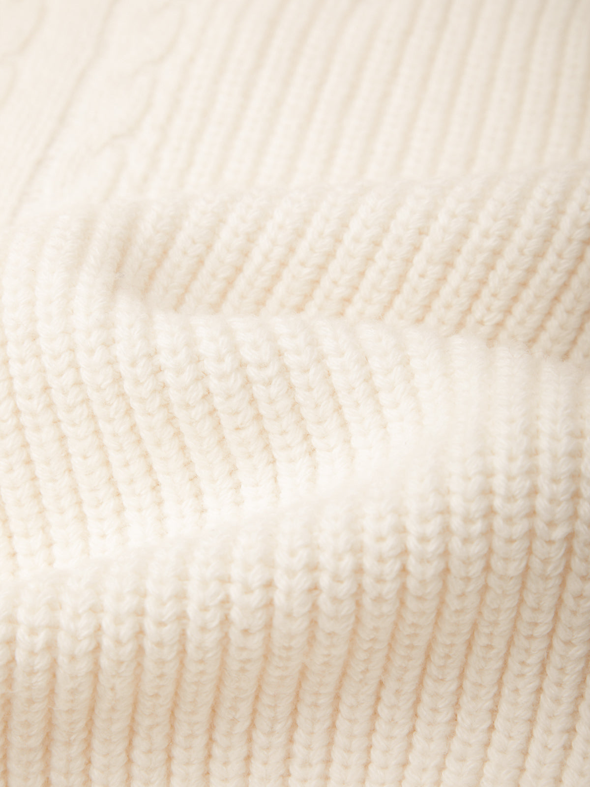 Close-up of a cream-colored ribbed knit fabric texture.