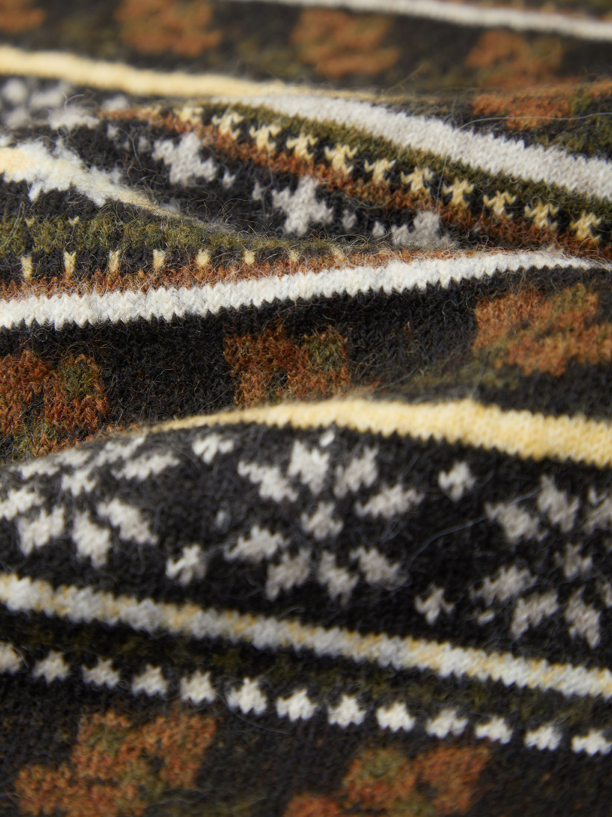Close-up of a knitted textile with a multicolor Fair Isle pattern featuring black, brown, white, and olive green yarns.