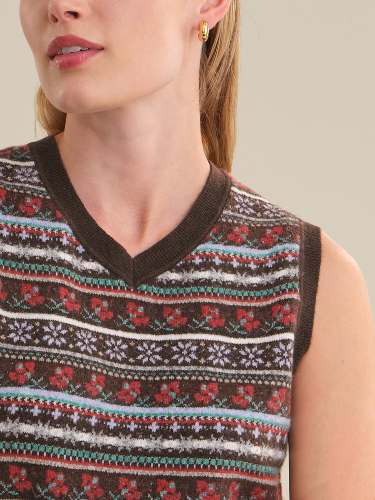 Close-up of a woman wearing a sleeveless knit sweater vest with a brown V-neck and a multicolor Fair Isle pattern featuring red, white, and teal stripes.