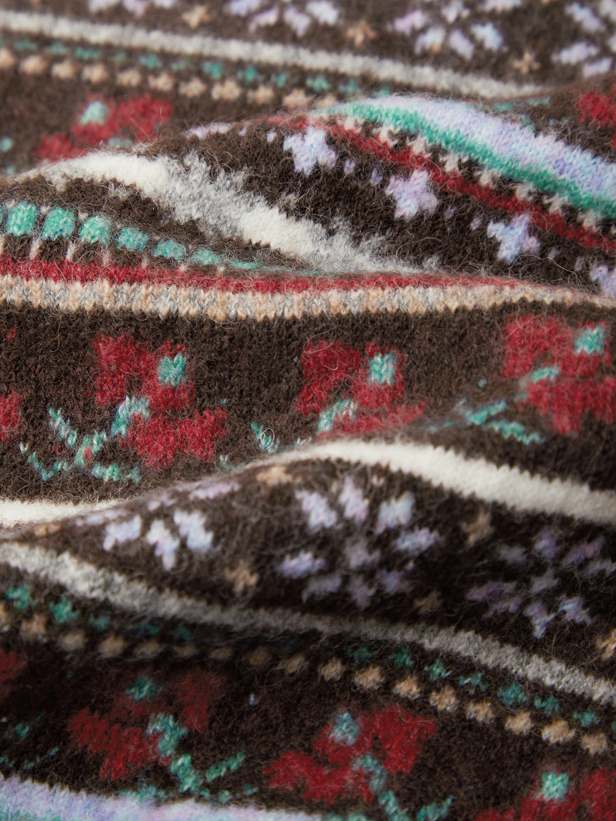 A close-up of a textured knit fabric with a multicolor Fair Isle pattern featuring dark brown, red, teal, cream, and white.