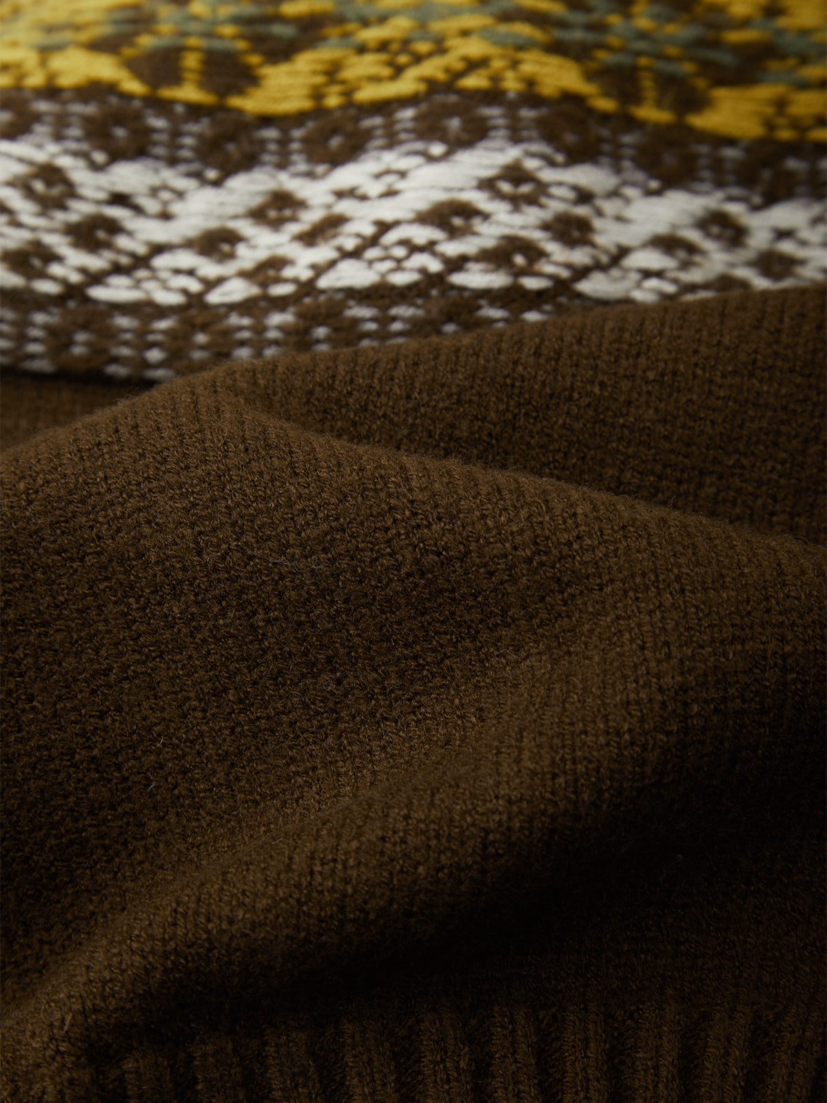 Close-up of a dark brown knit fabric with a patterned section showing yellow, white, and brown Fair Isle style detailing.