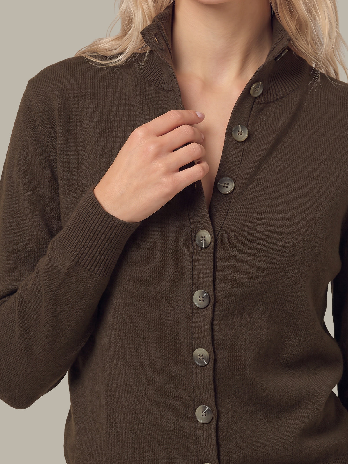 A close-up of a woman wearing a ribbed brown button-front cardigan sweater, with her hand adjusting the collar and buttons.