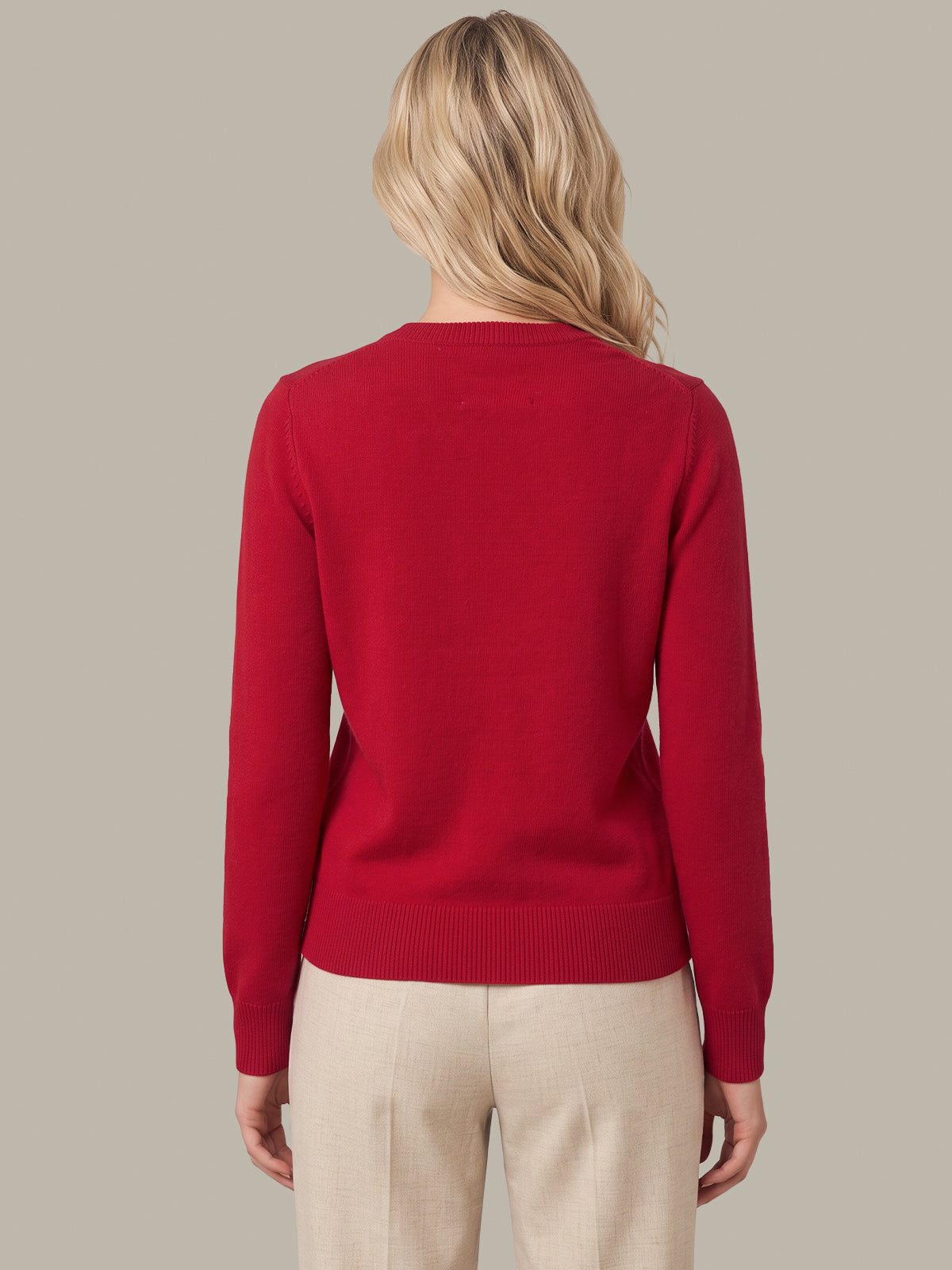 A woman viewed from the back wearing a solid red long-sleeve knit sweater and light beige trousers, set against a solid neutral gray background.