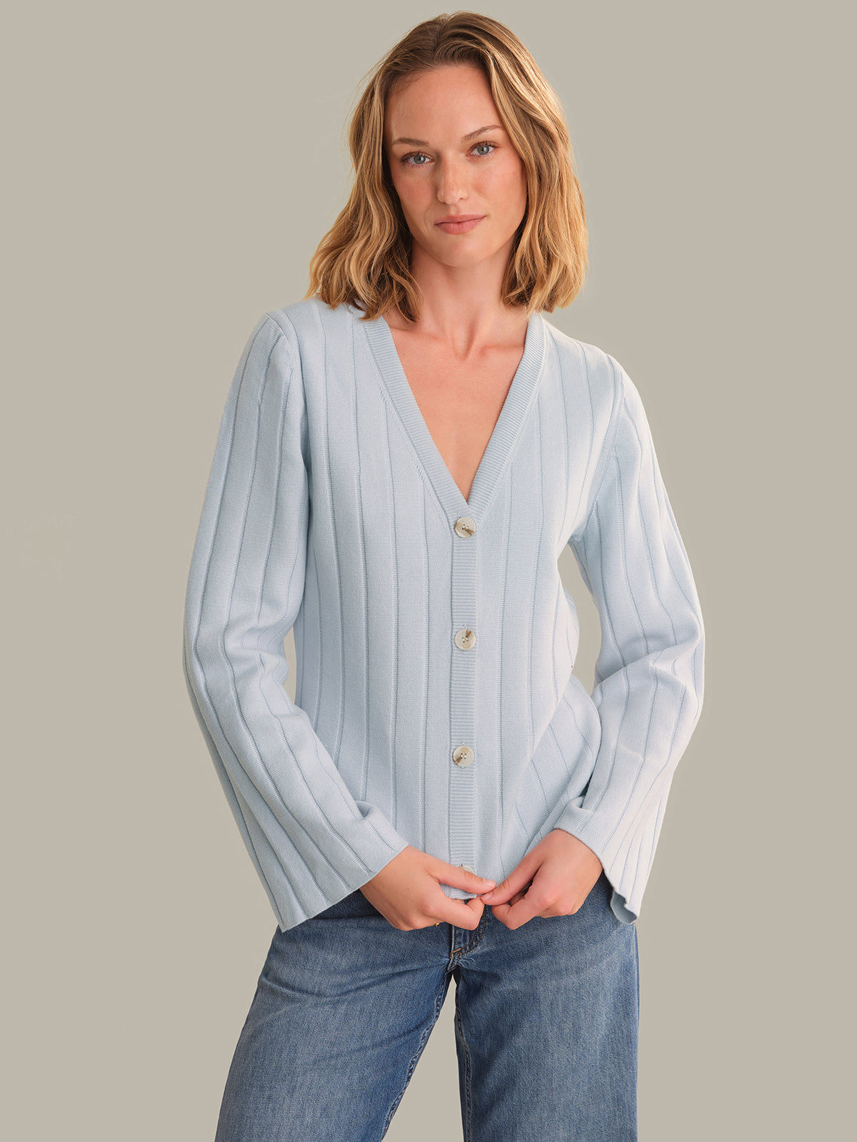 Woman wearing a light blue ribbed sweater with buttons and jeans on a gray background