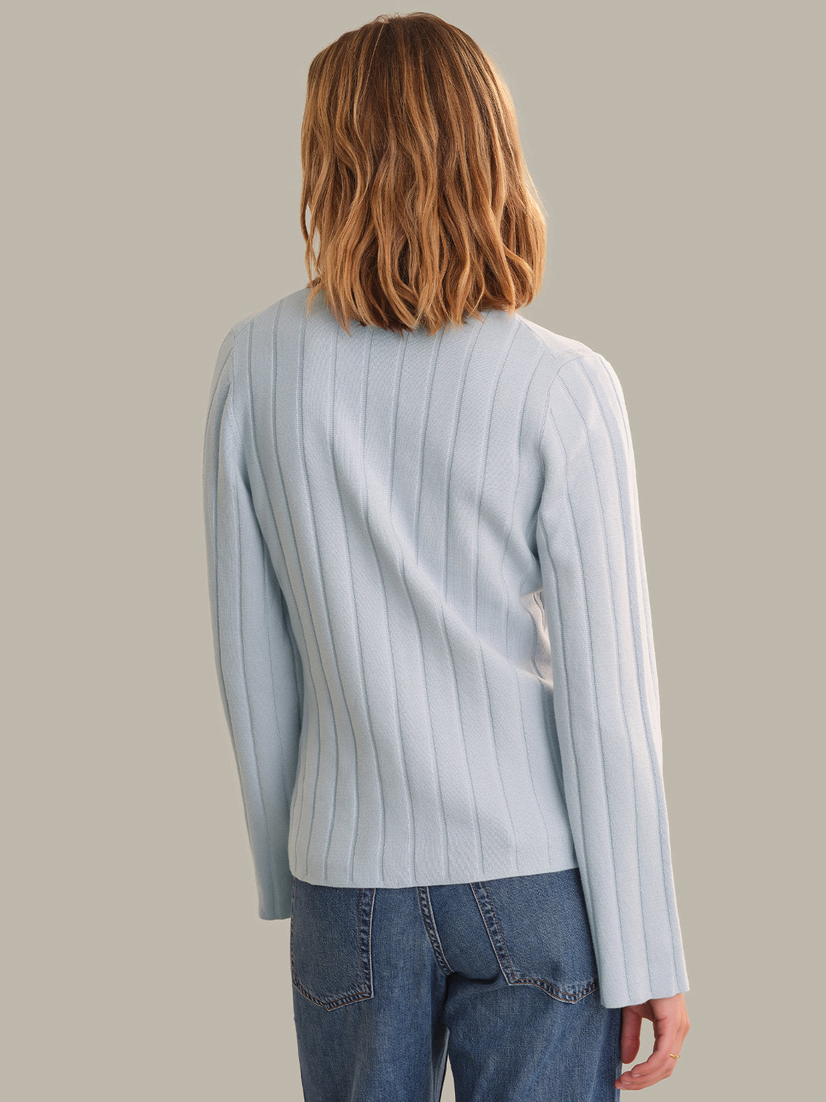 Person wearing a light blue ribbed sweater and jeans on a plain background